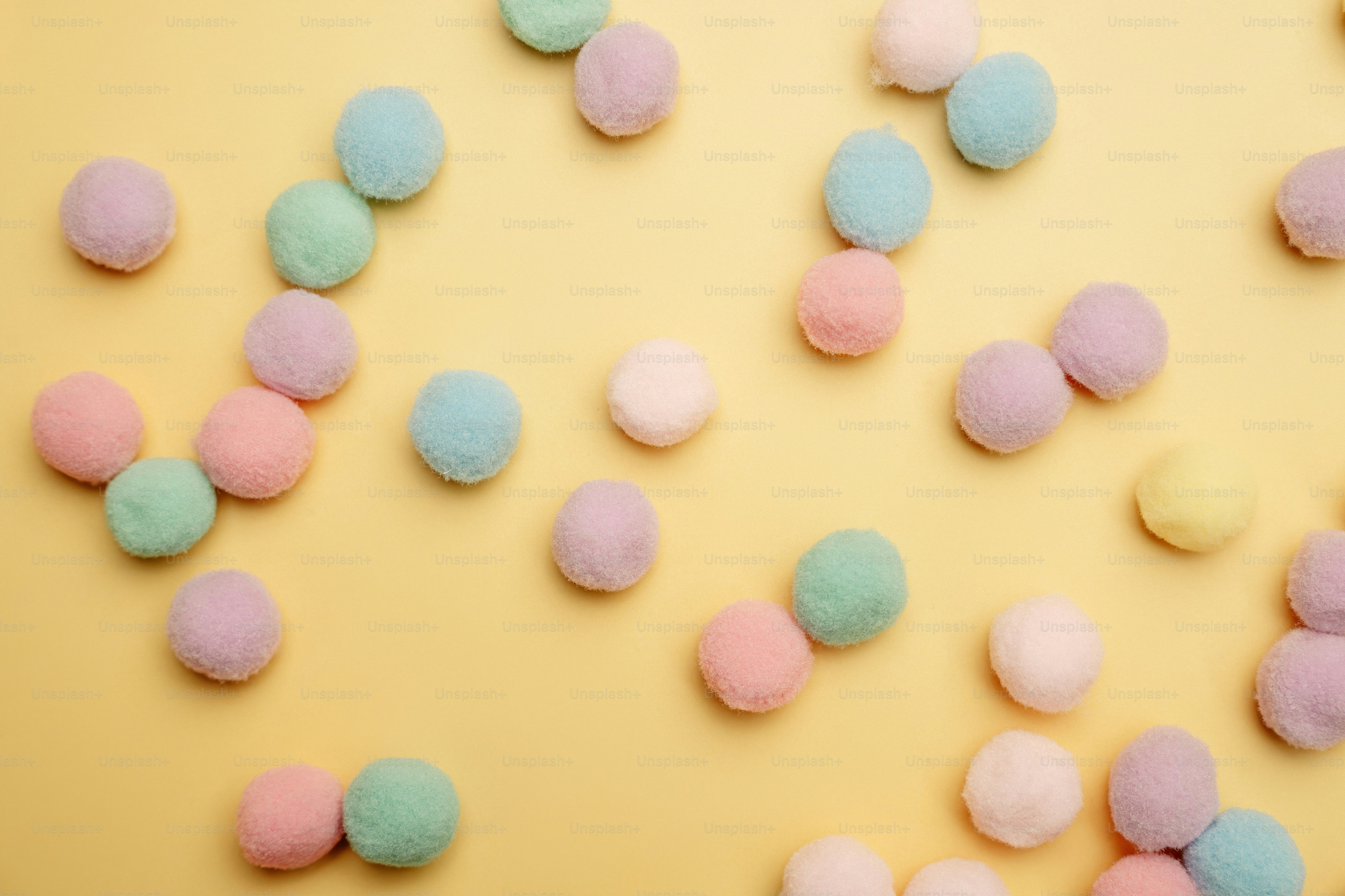 Pastel colored pom poms scattered on yellow background