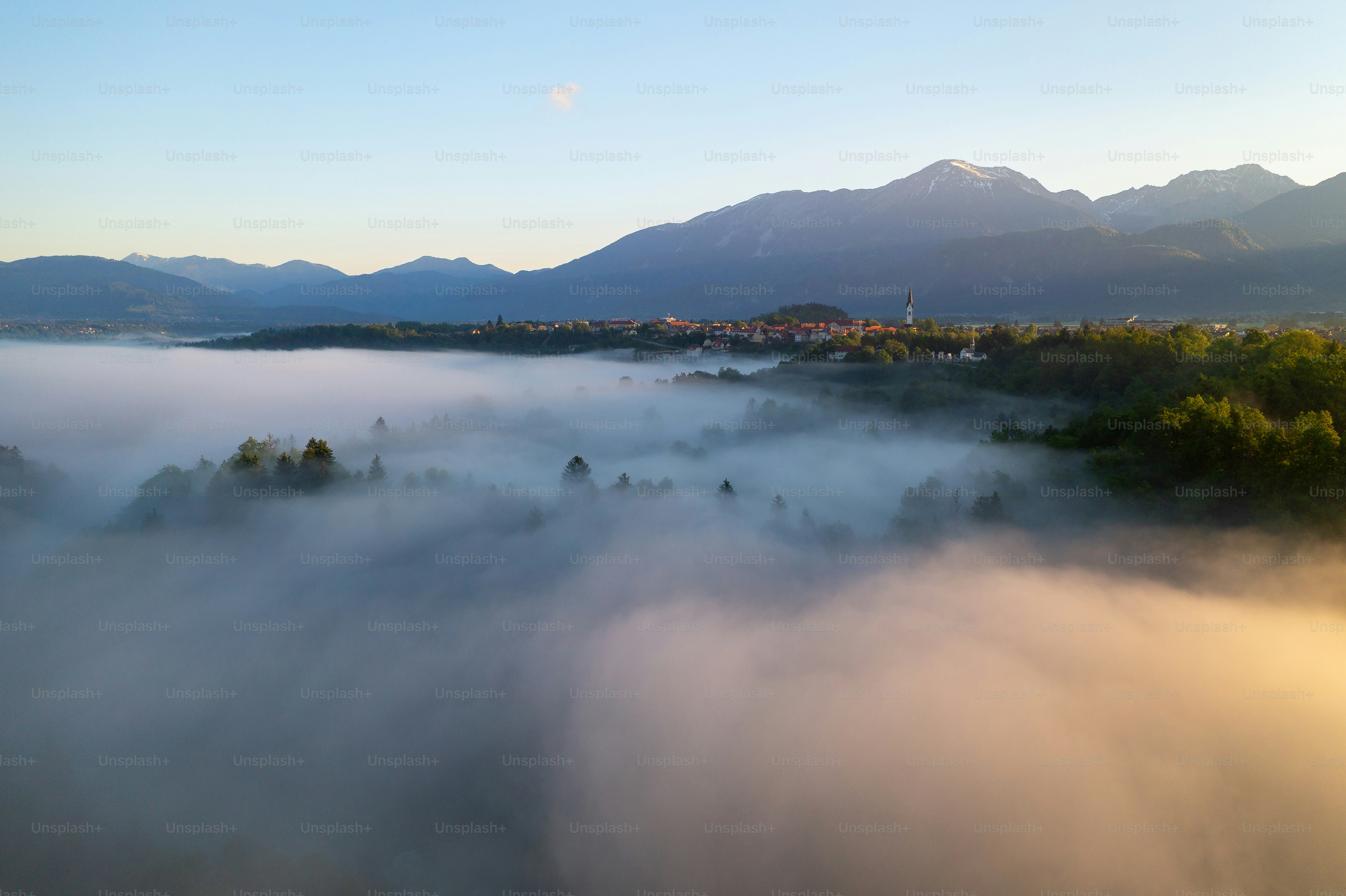 Nebliges Tal mit fernen Bergen und einem Dorf bei Sonnenaufgang.