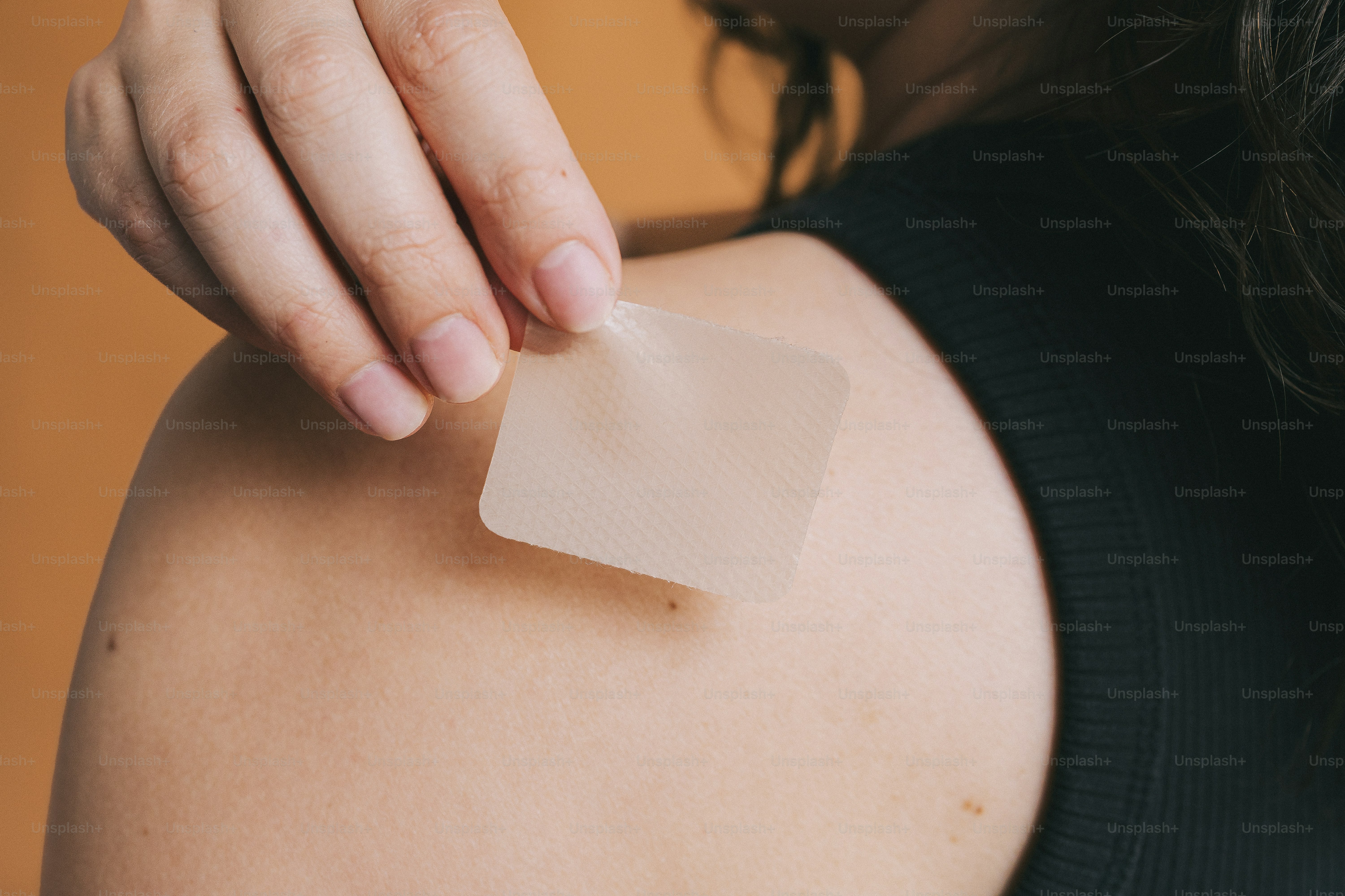 Person applying a small square patch to their shoulder.