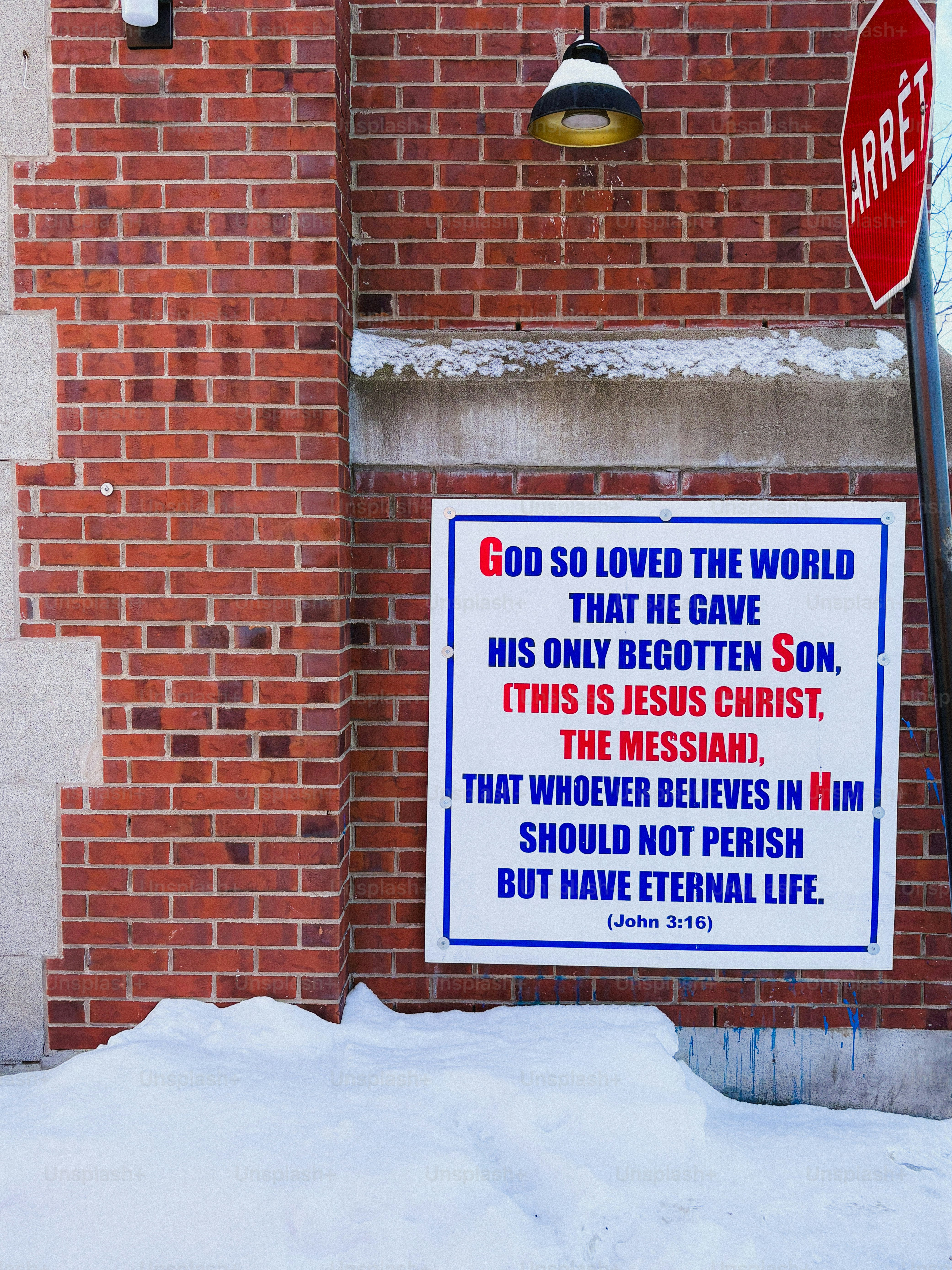 Religious text displayed on a brick wall with snow.