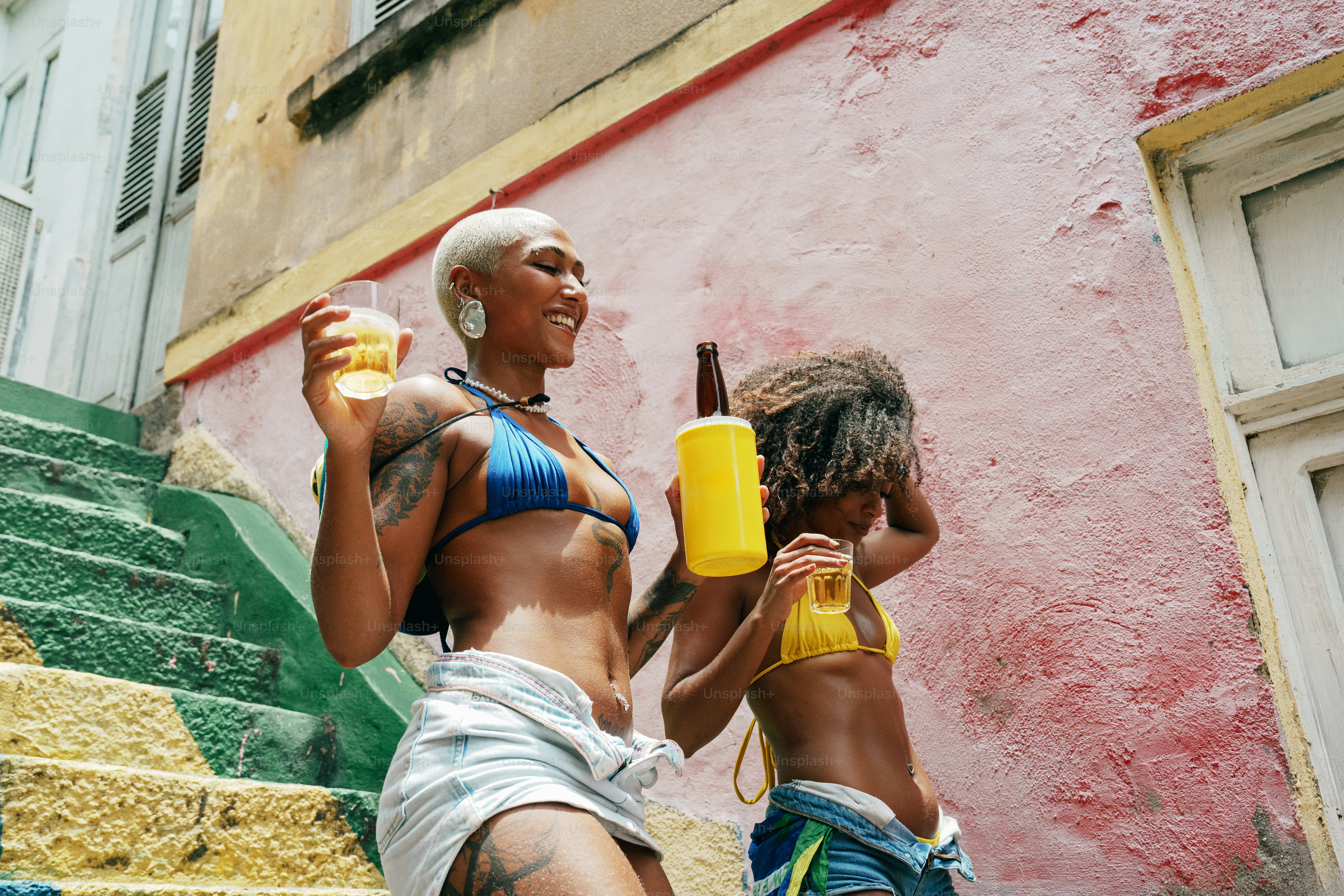 Zwei Frauen im Bikini halten Getränke auf der Treppe.