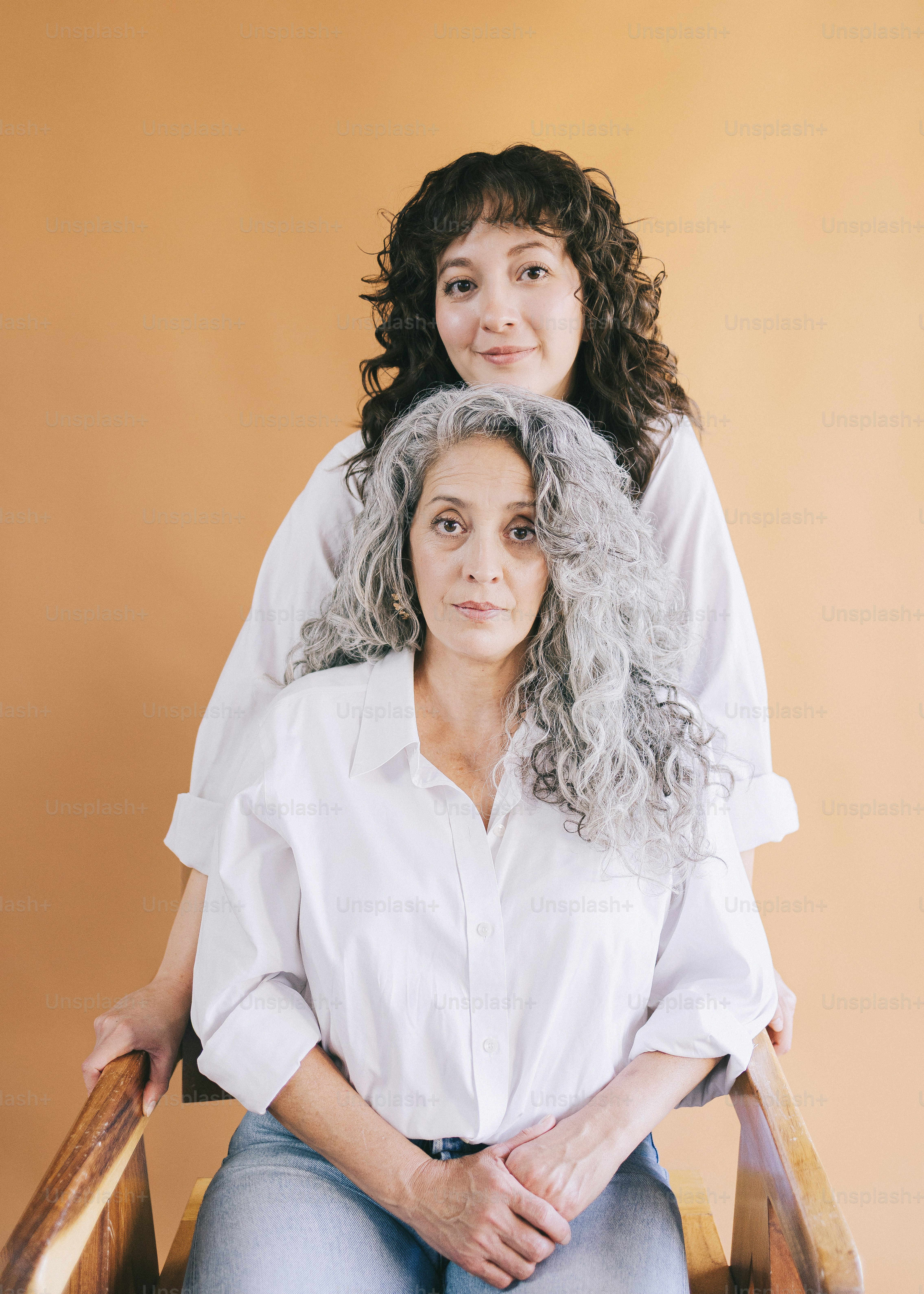 Two women with white shirts on a tan background