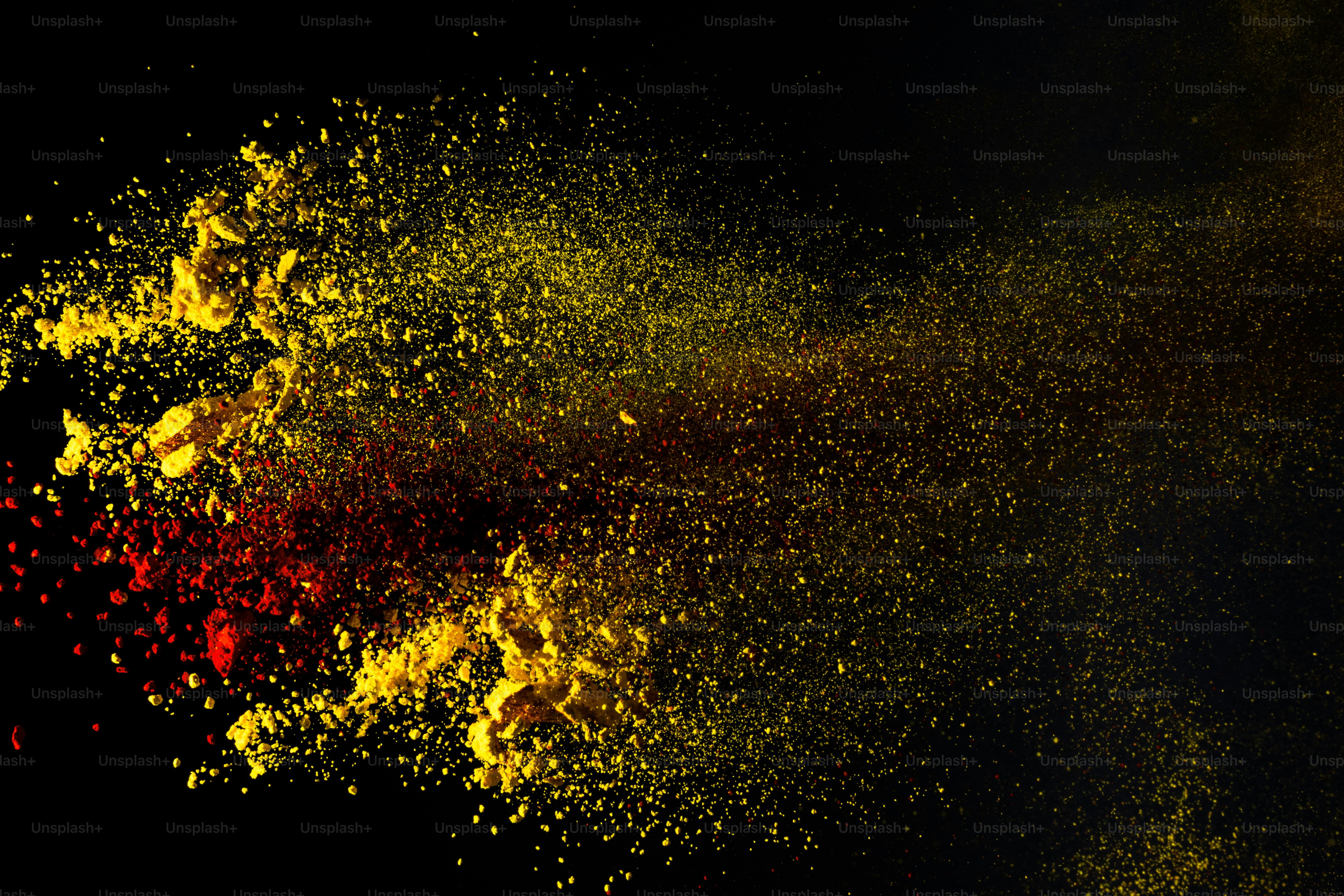 Yellow and red powder exploding against a black background photo ...