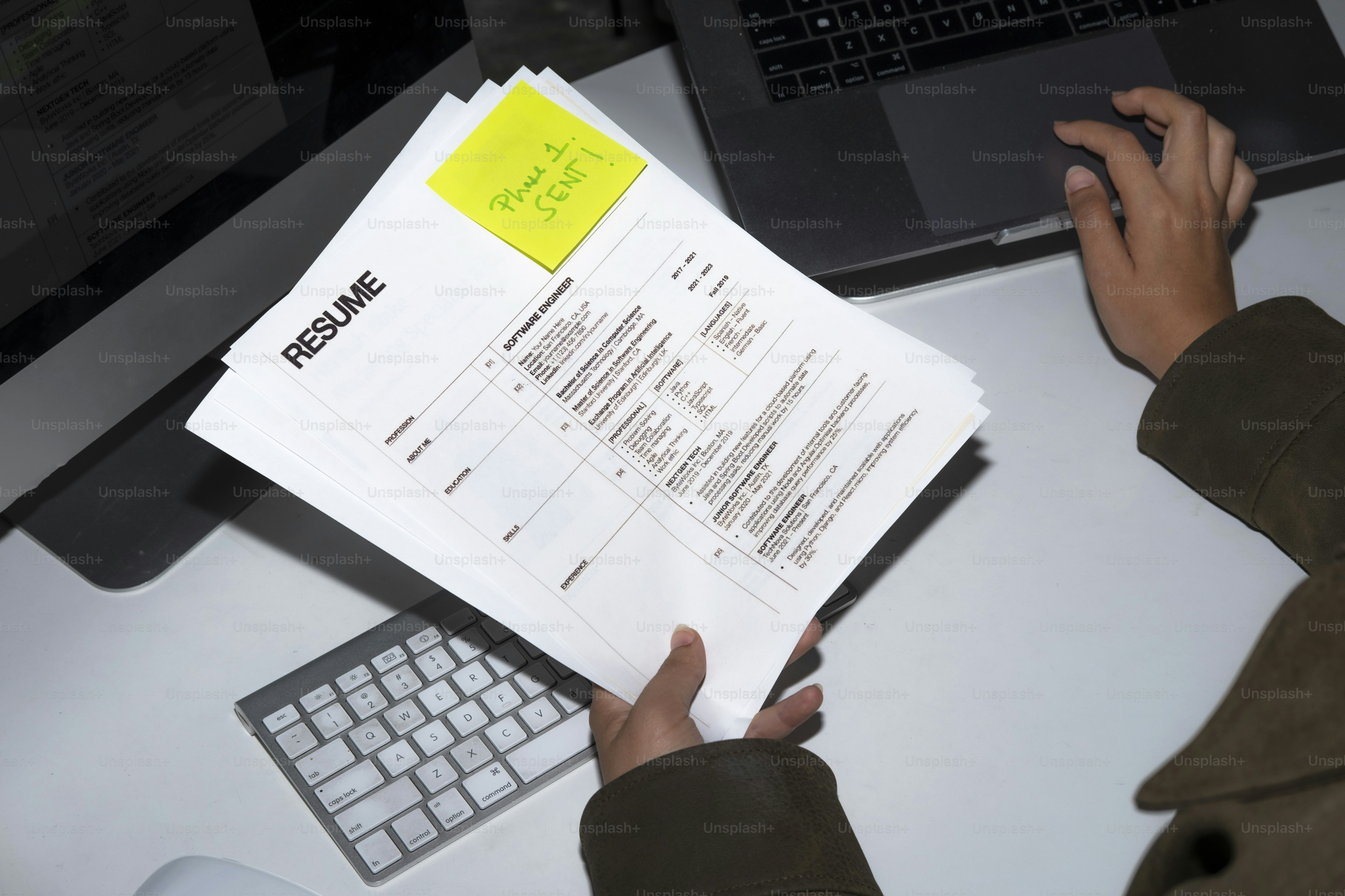 Hands holding resumes near laptop and computer.