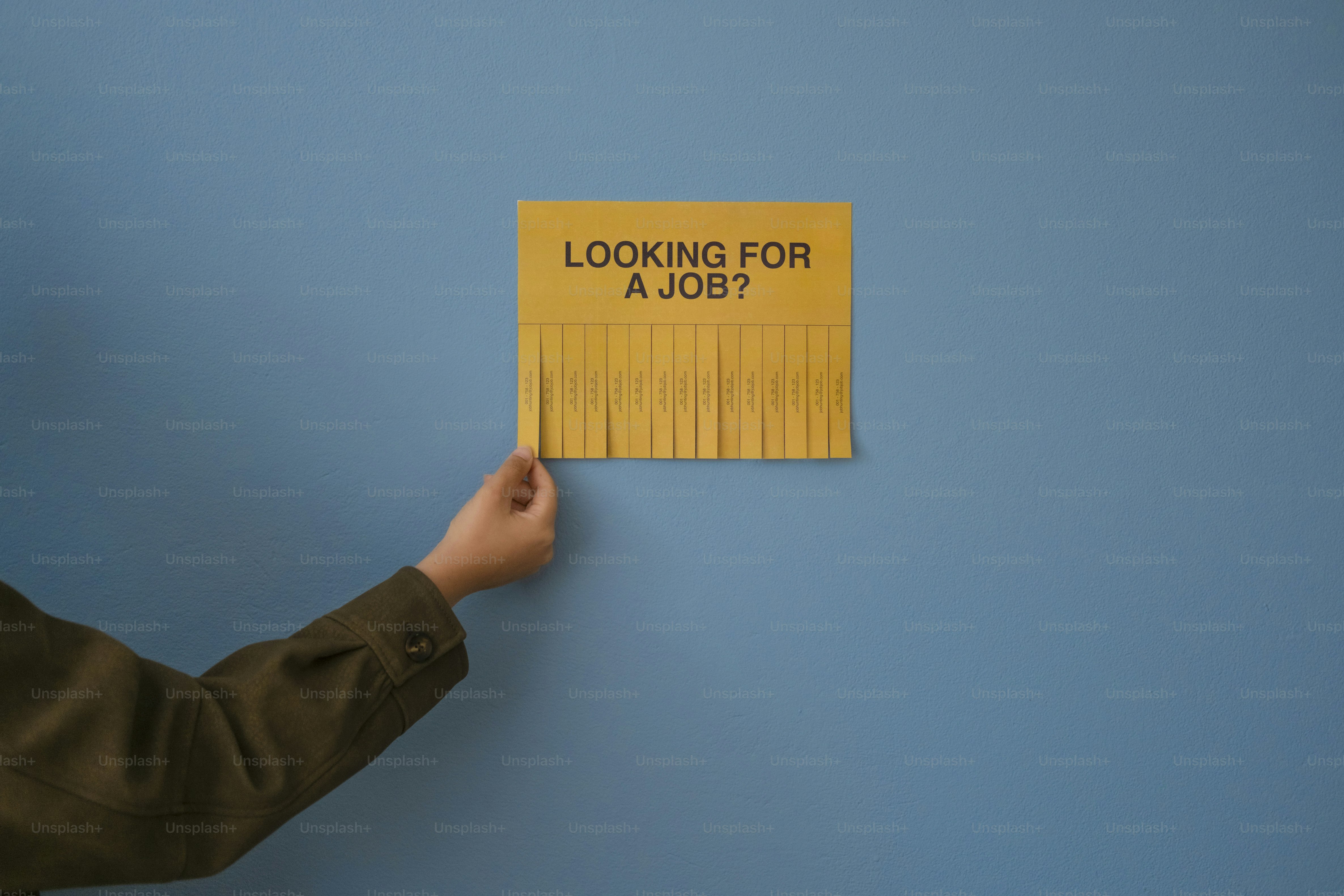 Una mano arrancando un folleto de '¿buscas trabajo?'.