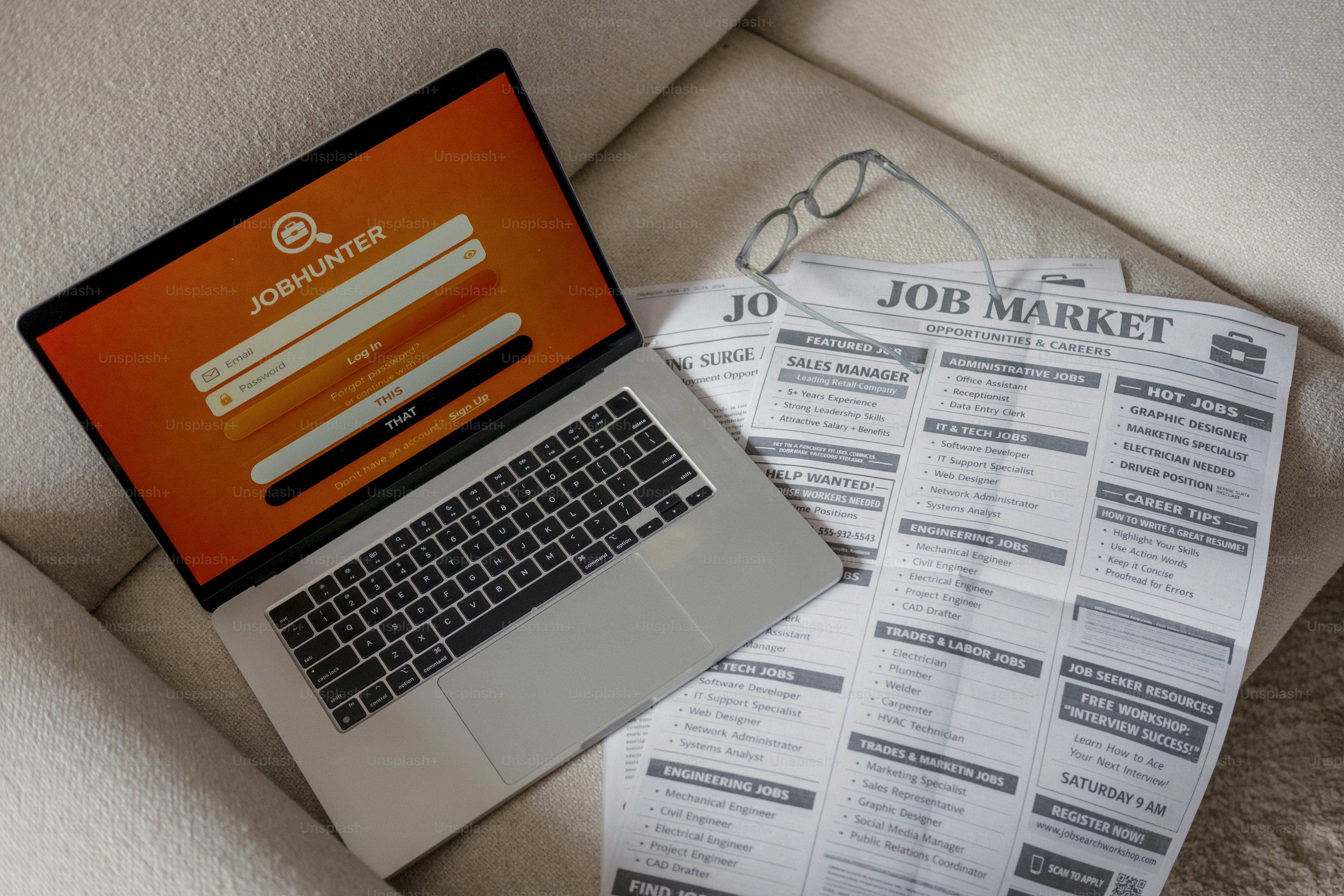 Laptop and newspaper with job listings on couch