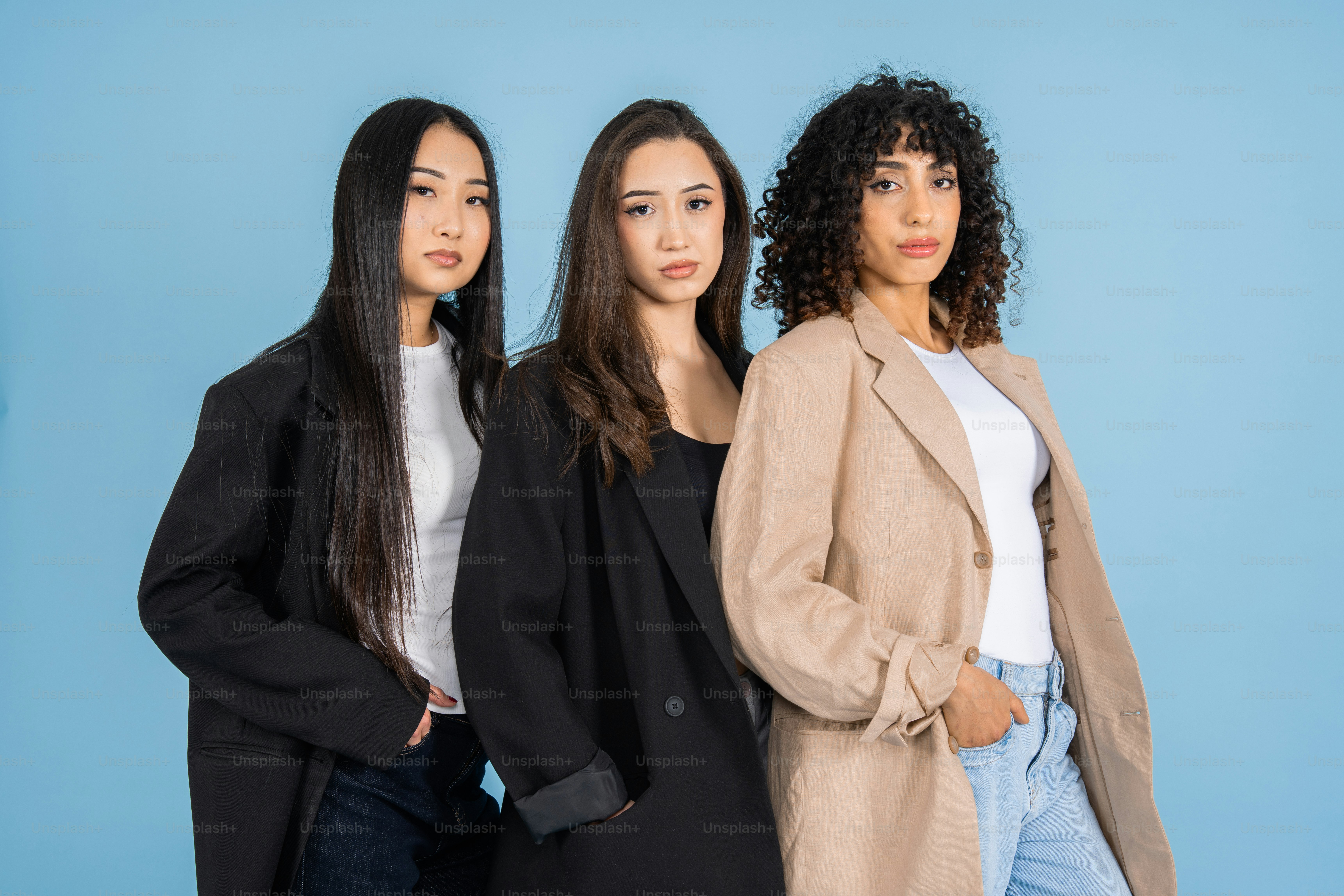 Trois femmes en veston se tiennent sur fond bleu