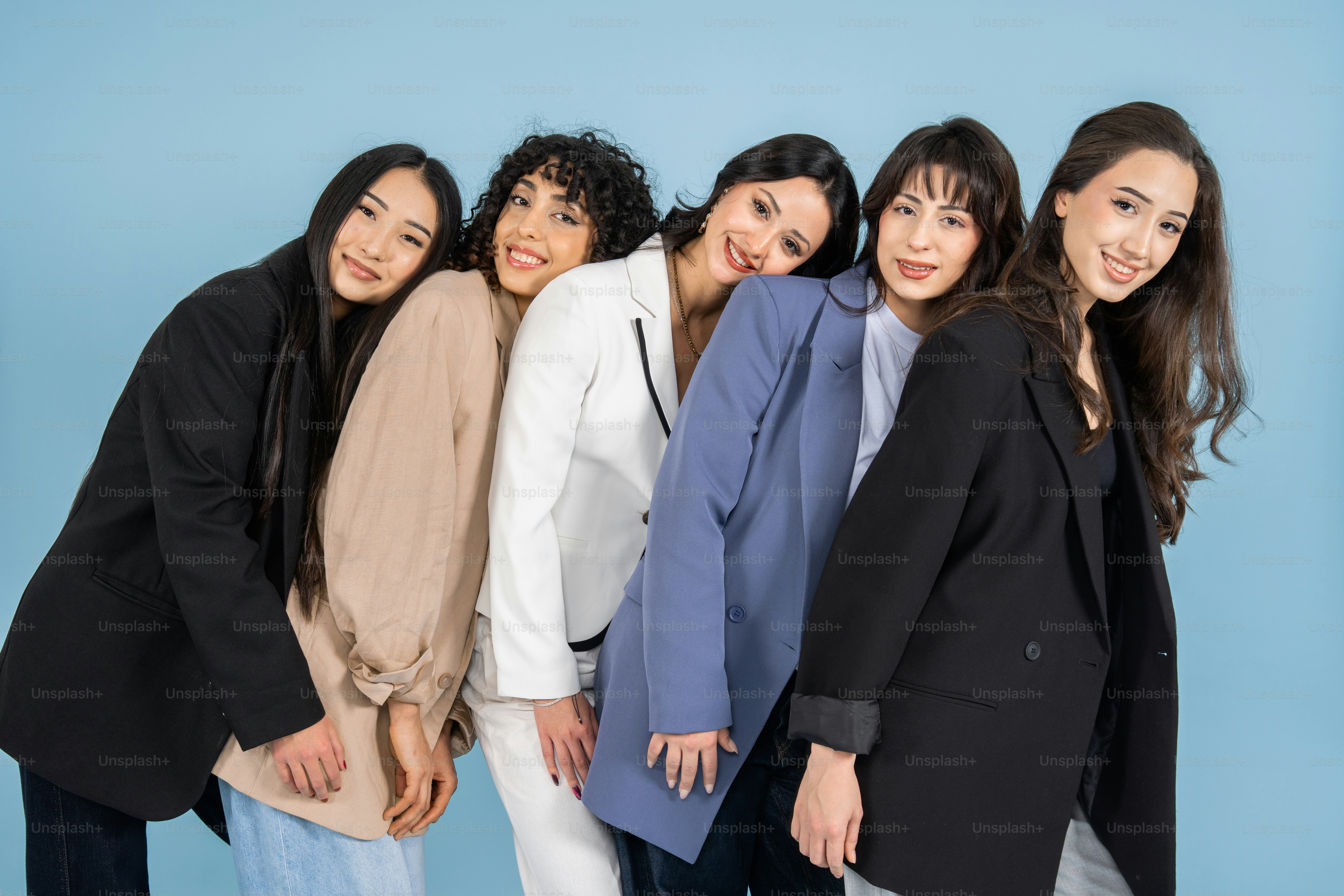 青い背景にブレザー姿の5人の女性が一緒に立っています
