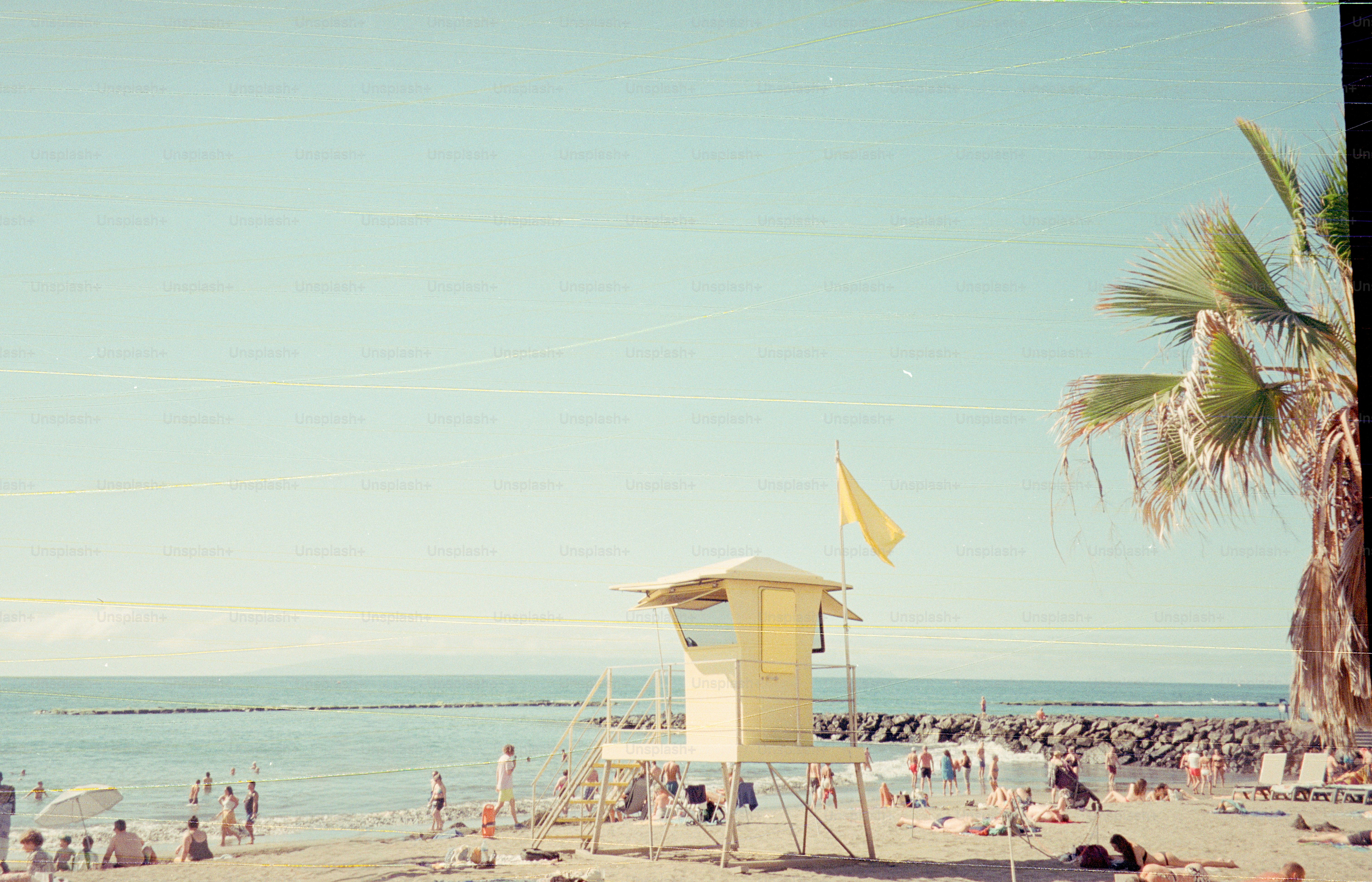 Menara penjaga pantai kuning di pantai yang ramai dengan pohon palem.