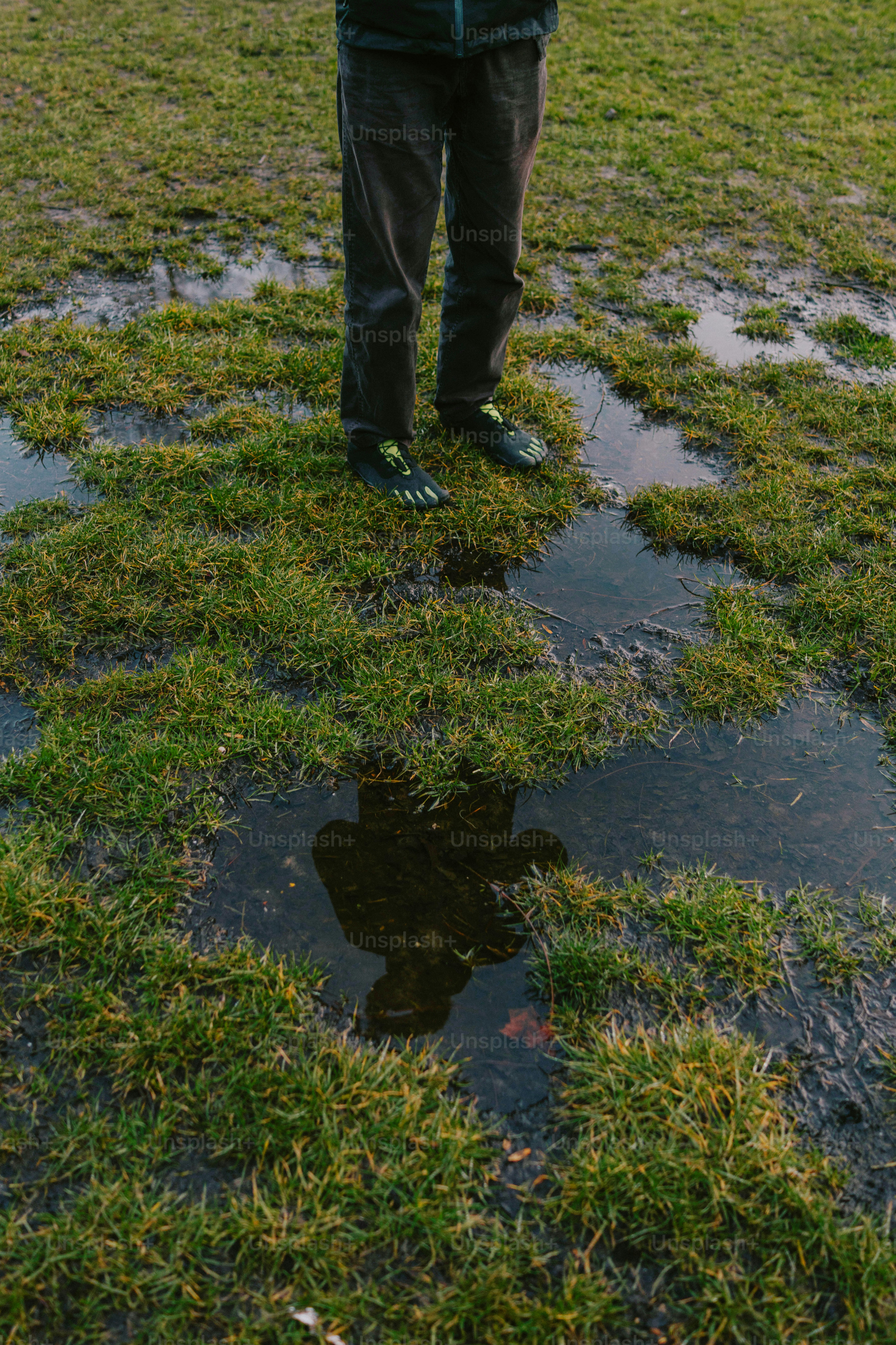 Person standing in a grassy field with puddles.