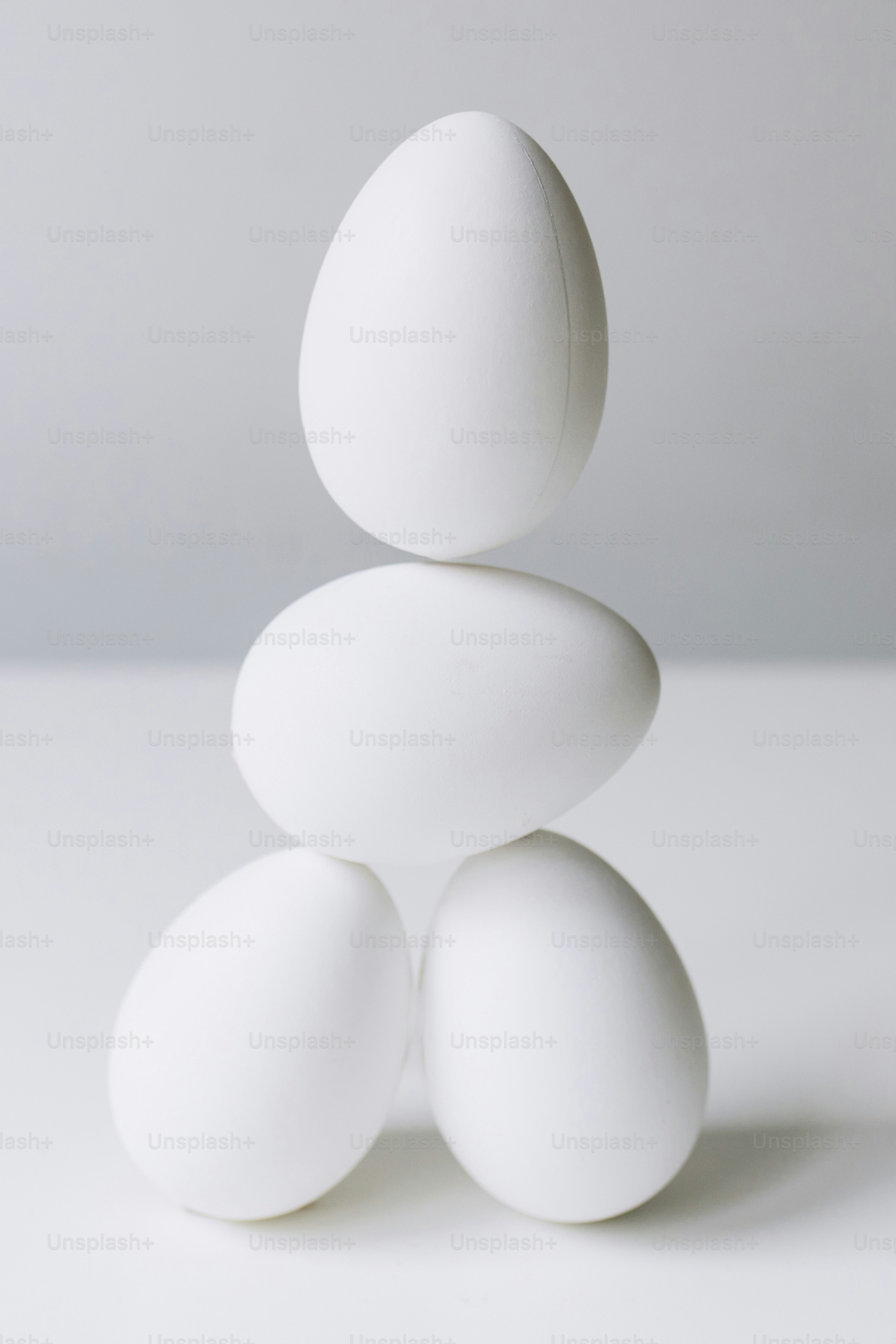 Quattro uova bianche impilate su una superficie bianca.