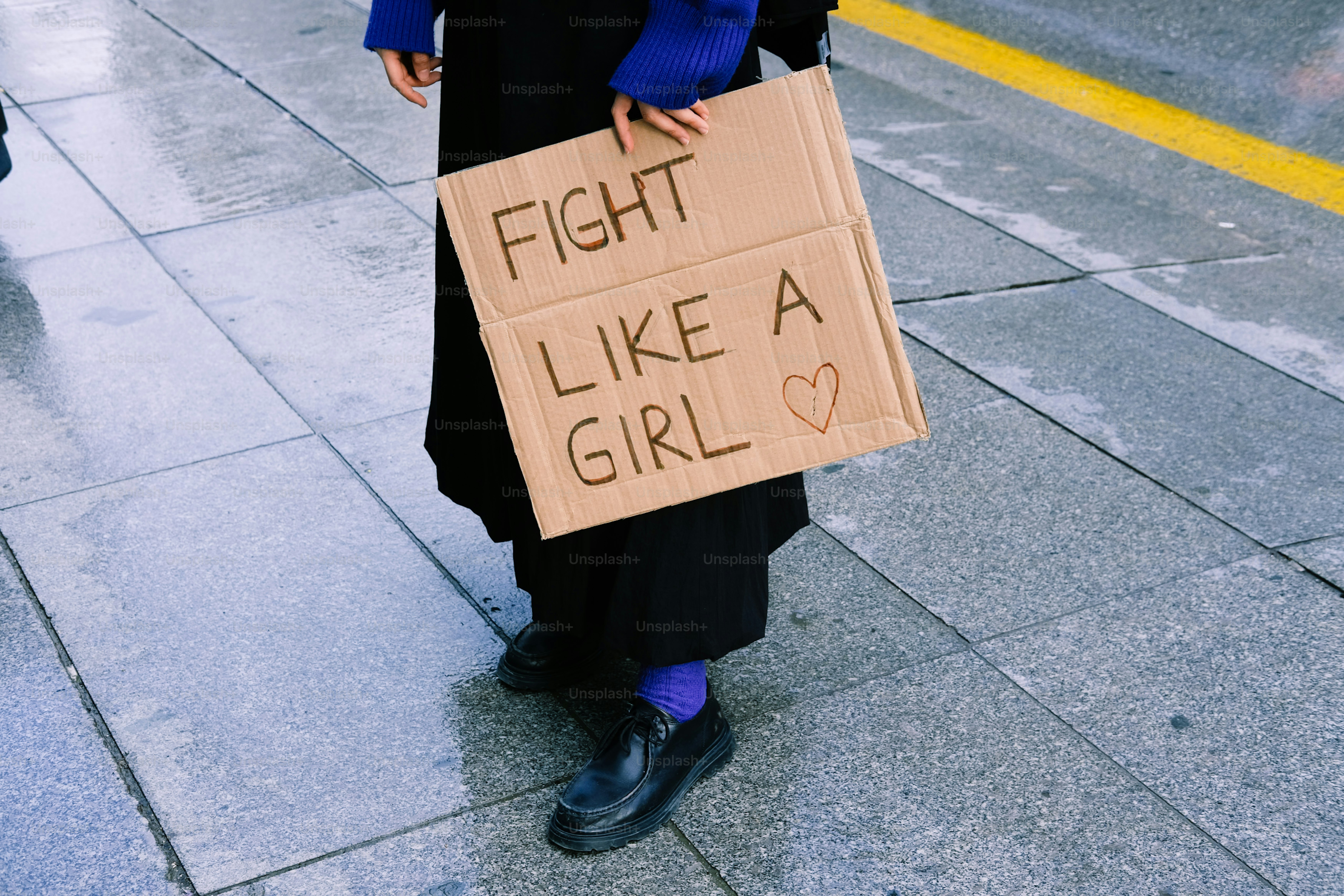 Une personne tient une pancarte en carton sur laquelle il est écrit « bats-toi comme une fille »