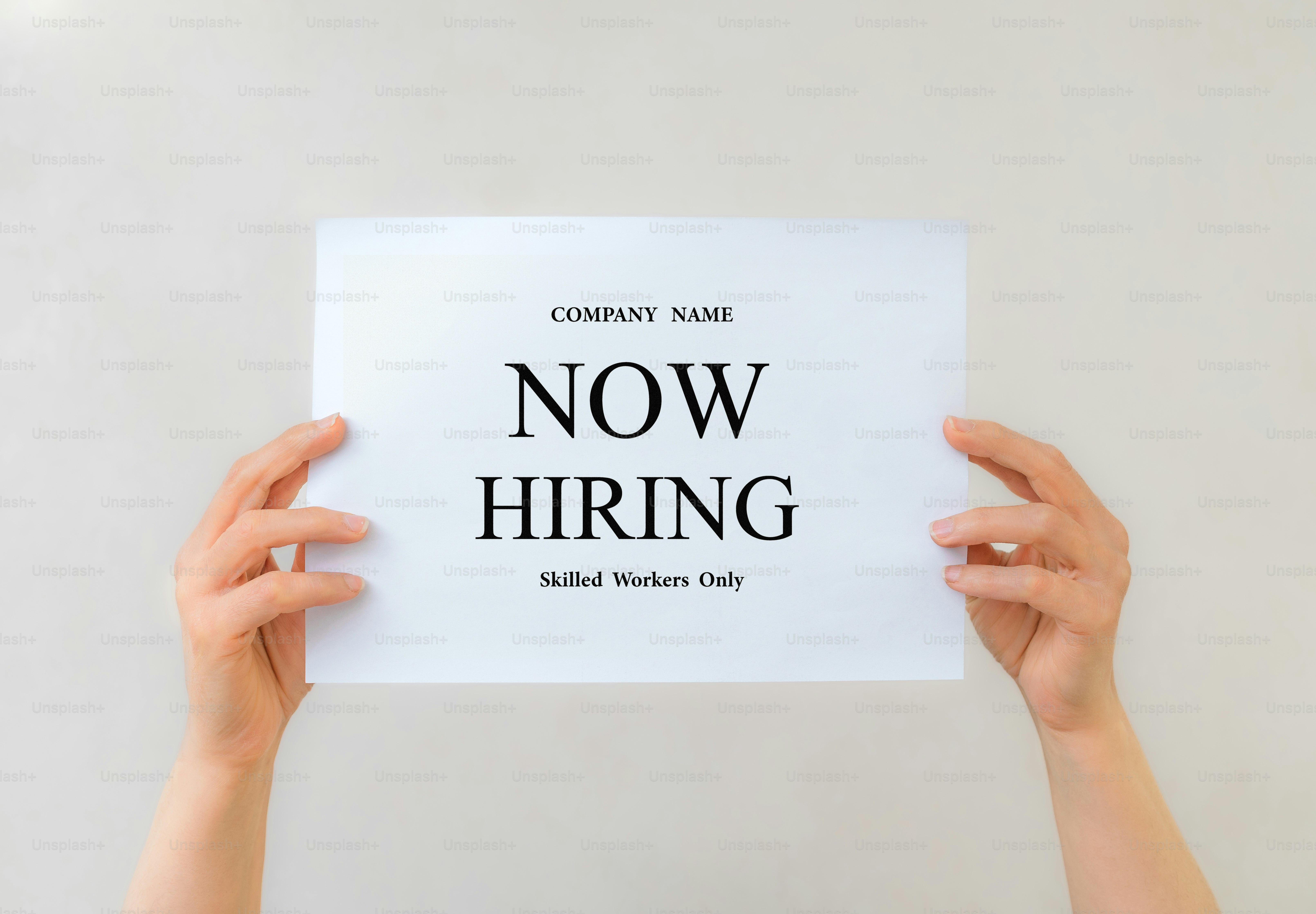 Hands holding a sign that says now hiring
