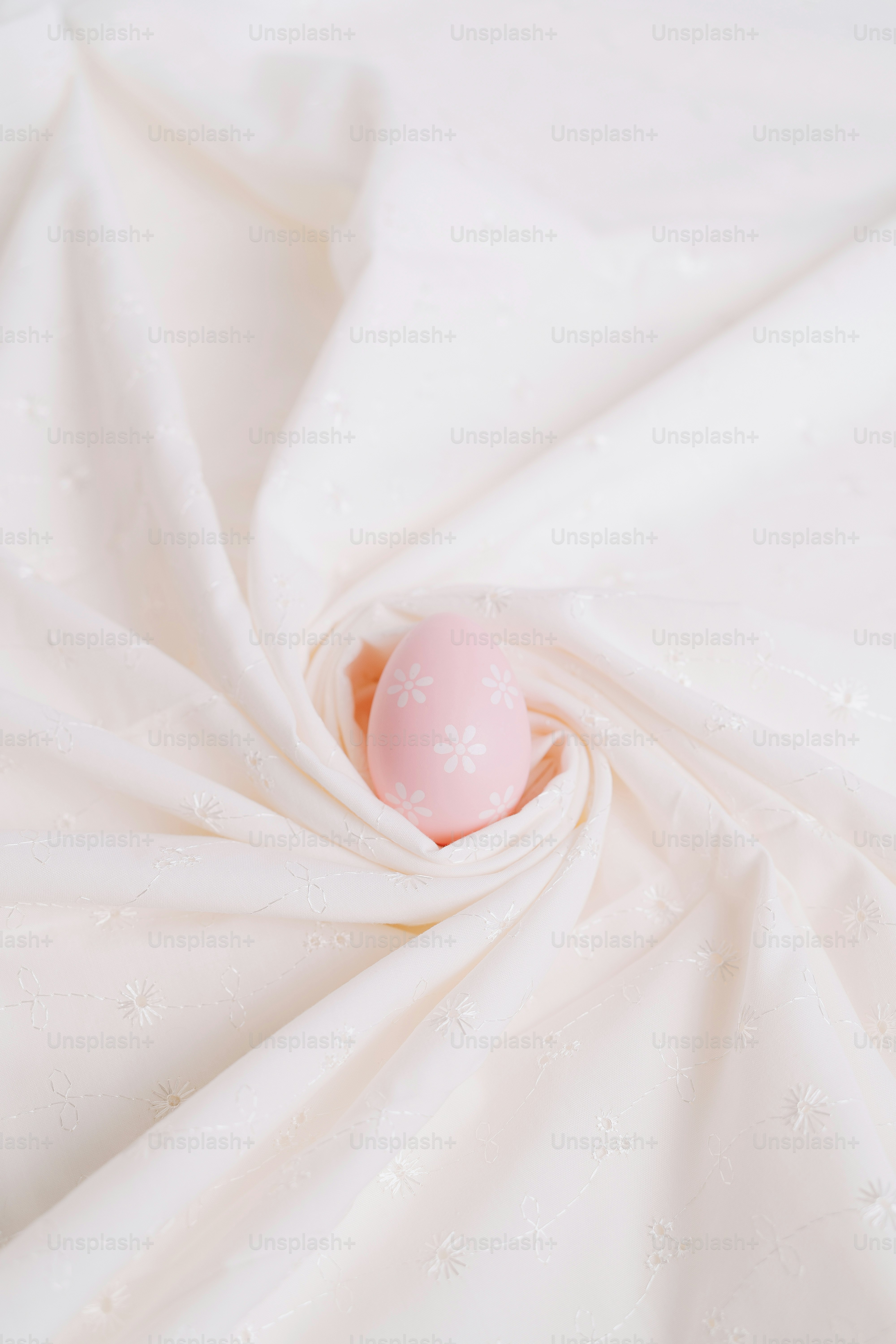 A pink easter egg rests on white fabric.