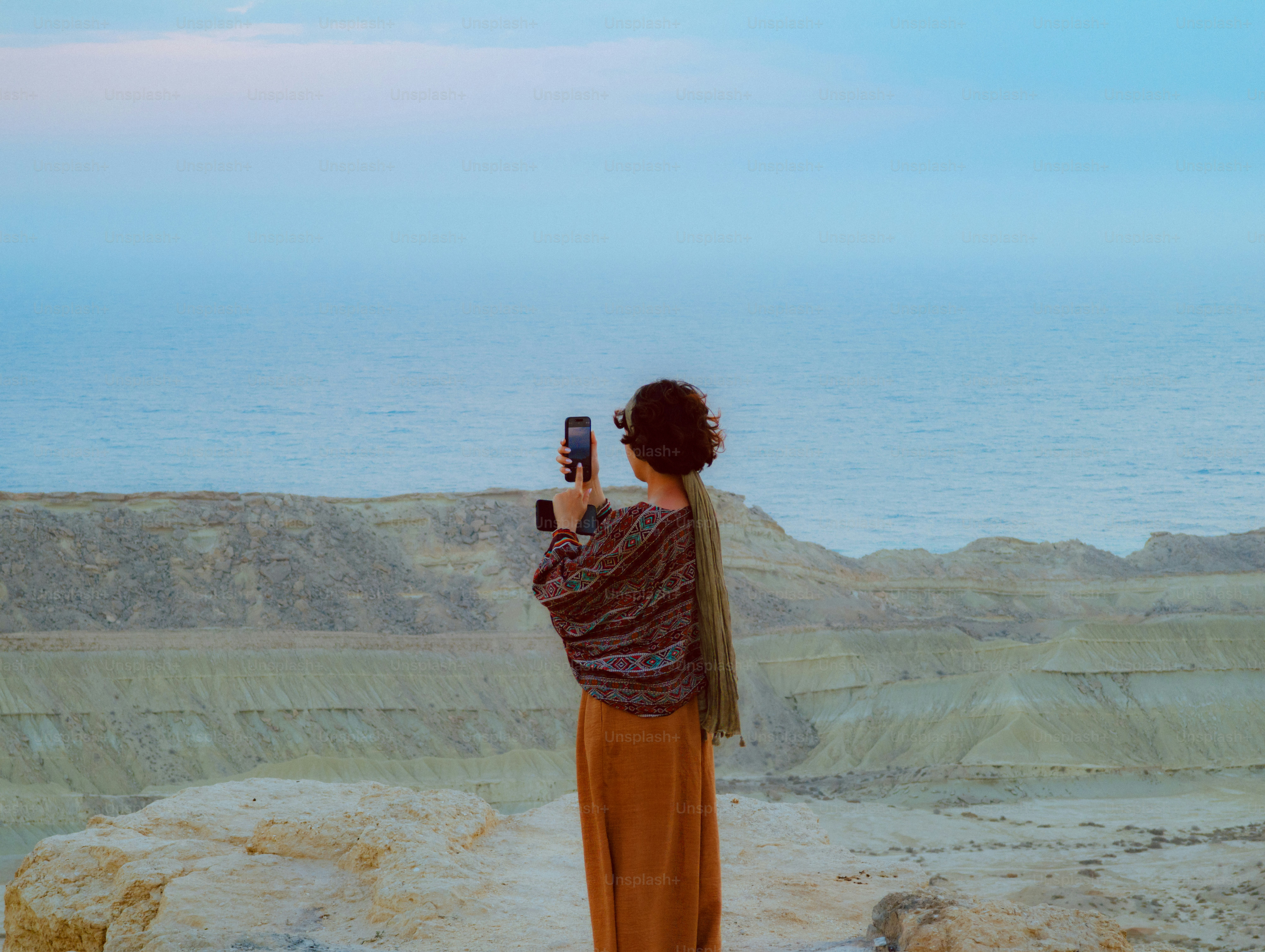 Woman taking a photo with her phone on a cliff.