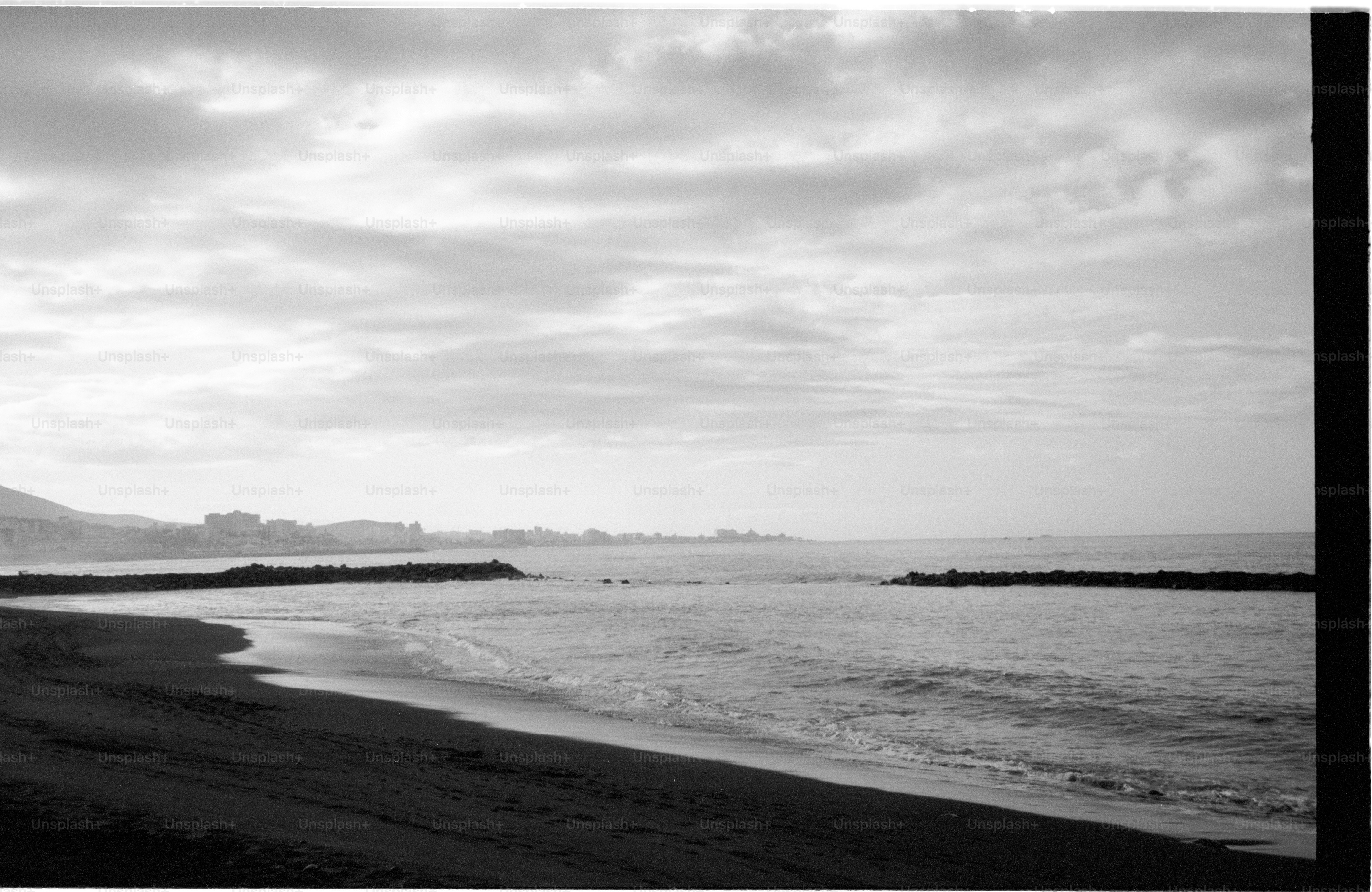 Calm ocean waves lap a sandy beach under cloudy sky.