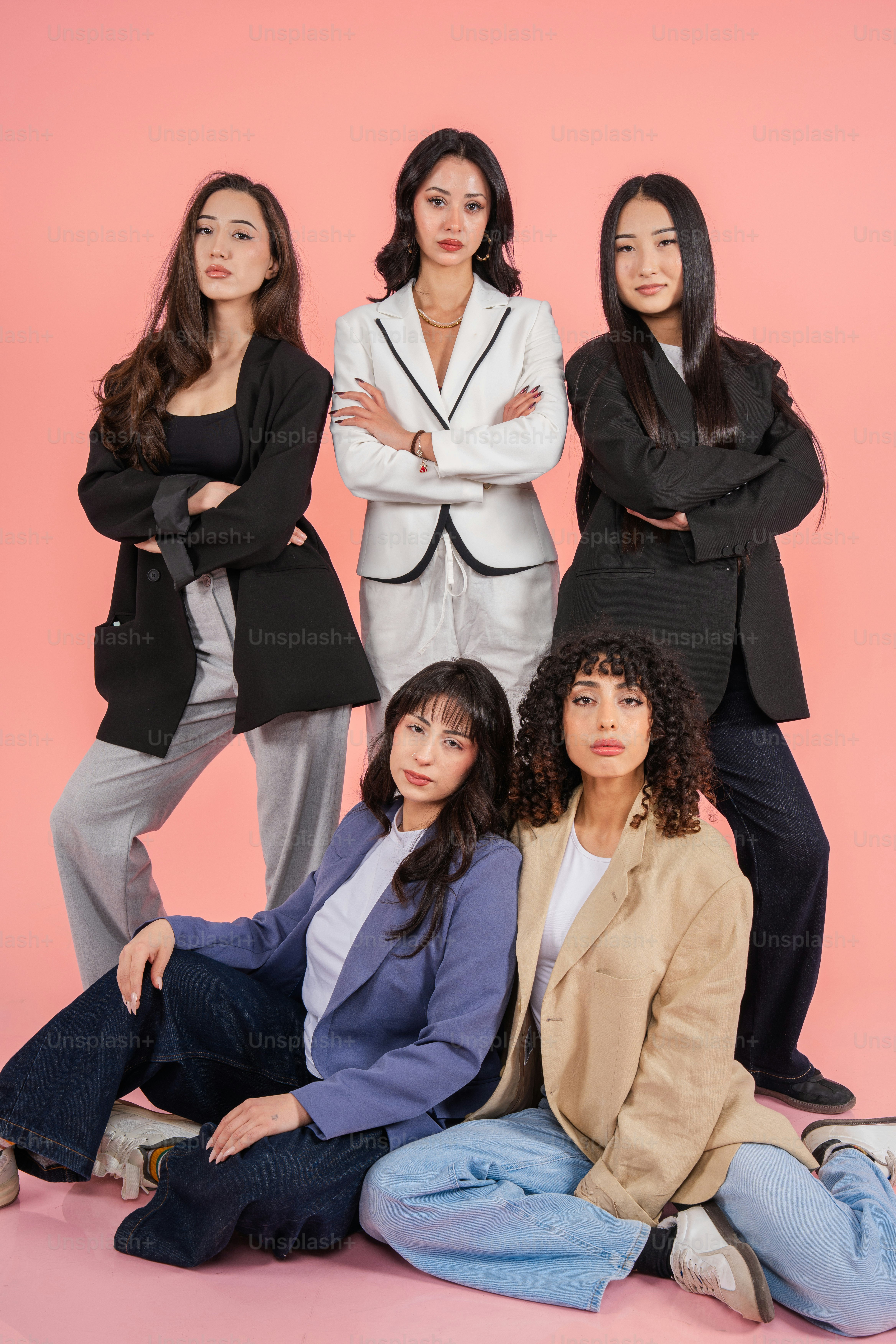 Five women in business attire posing against a pink background