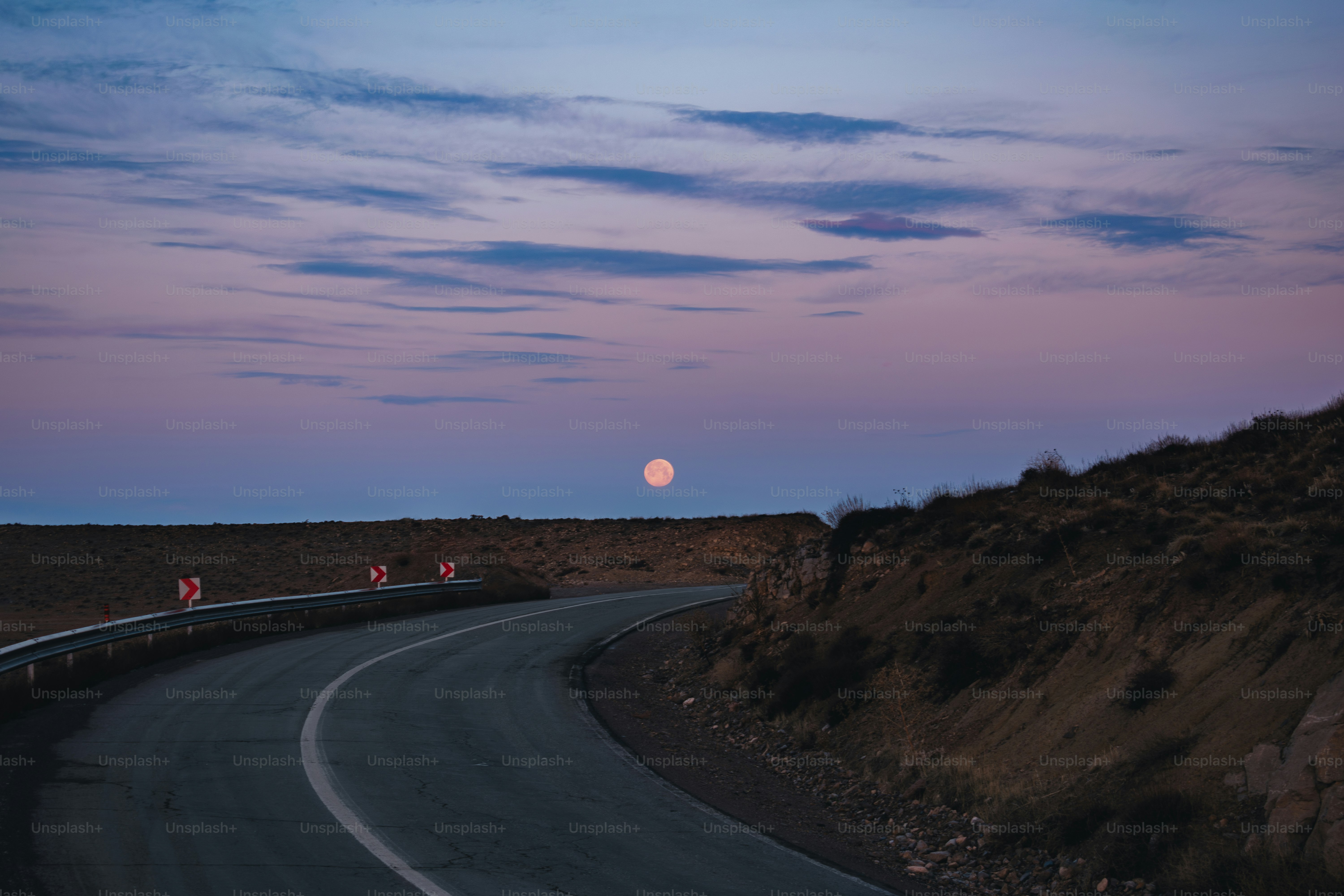Route sinueuse sous un ciel crépusculaire avec une pleine lune.