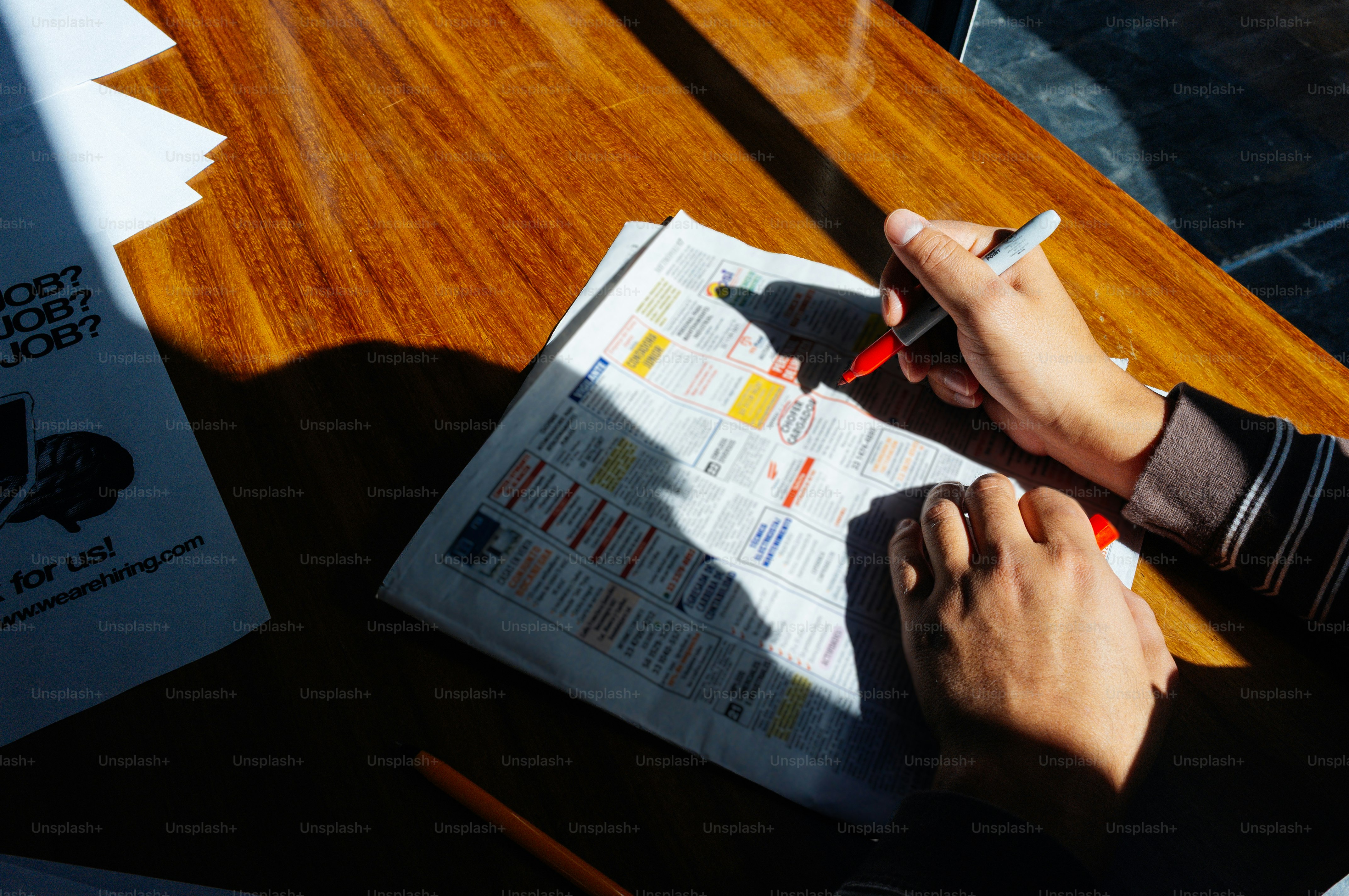 Des mains marquant un journal avec un stylo rouge.