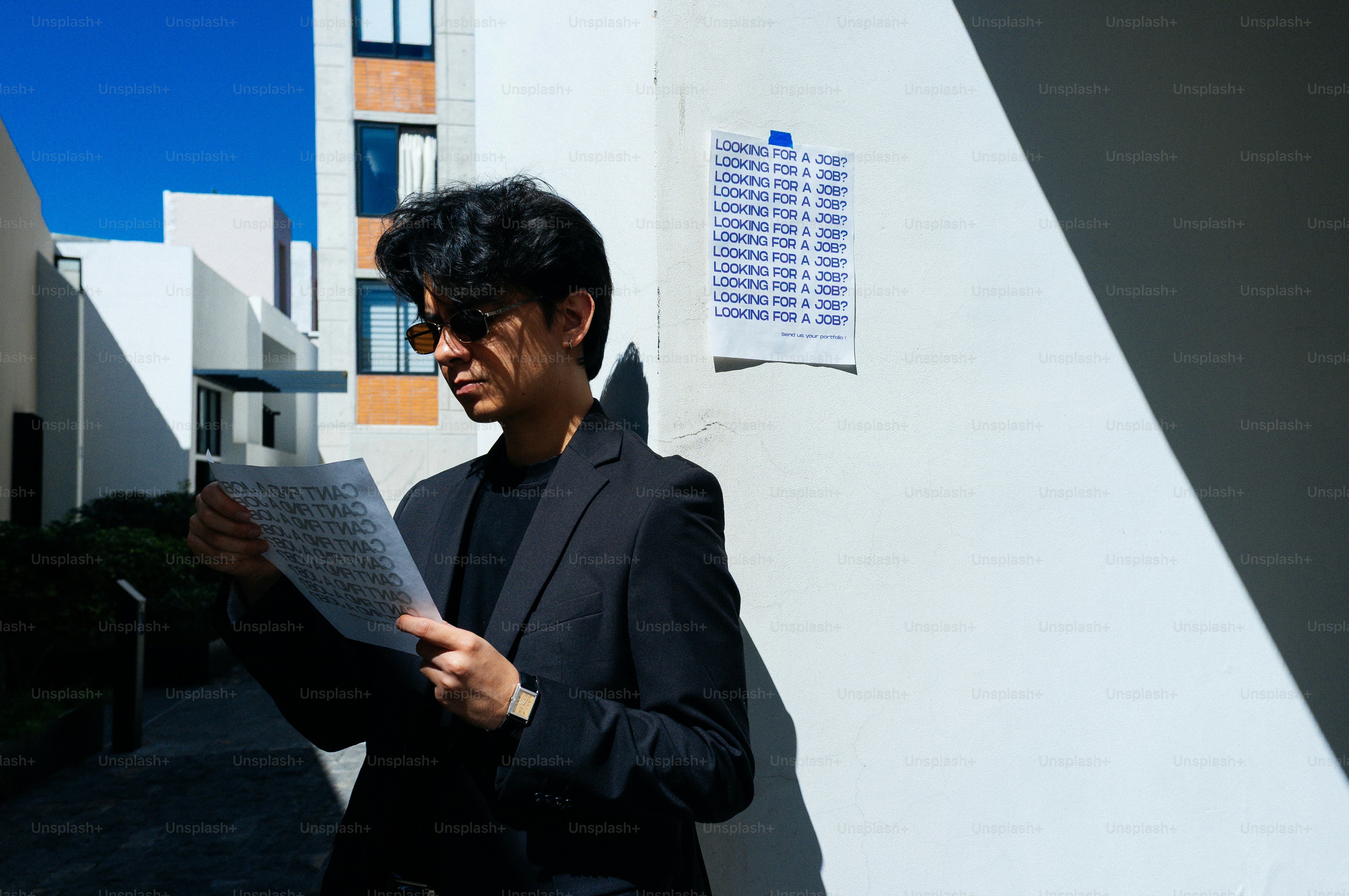 Un homme en costume lit des papiers près d’un mur blanc.