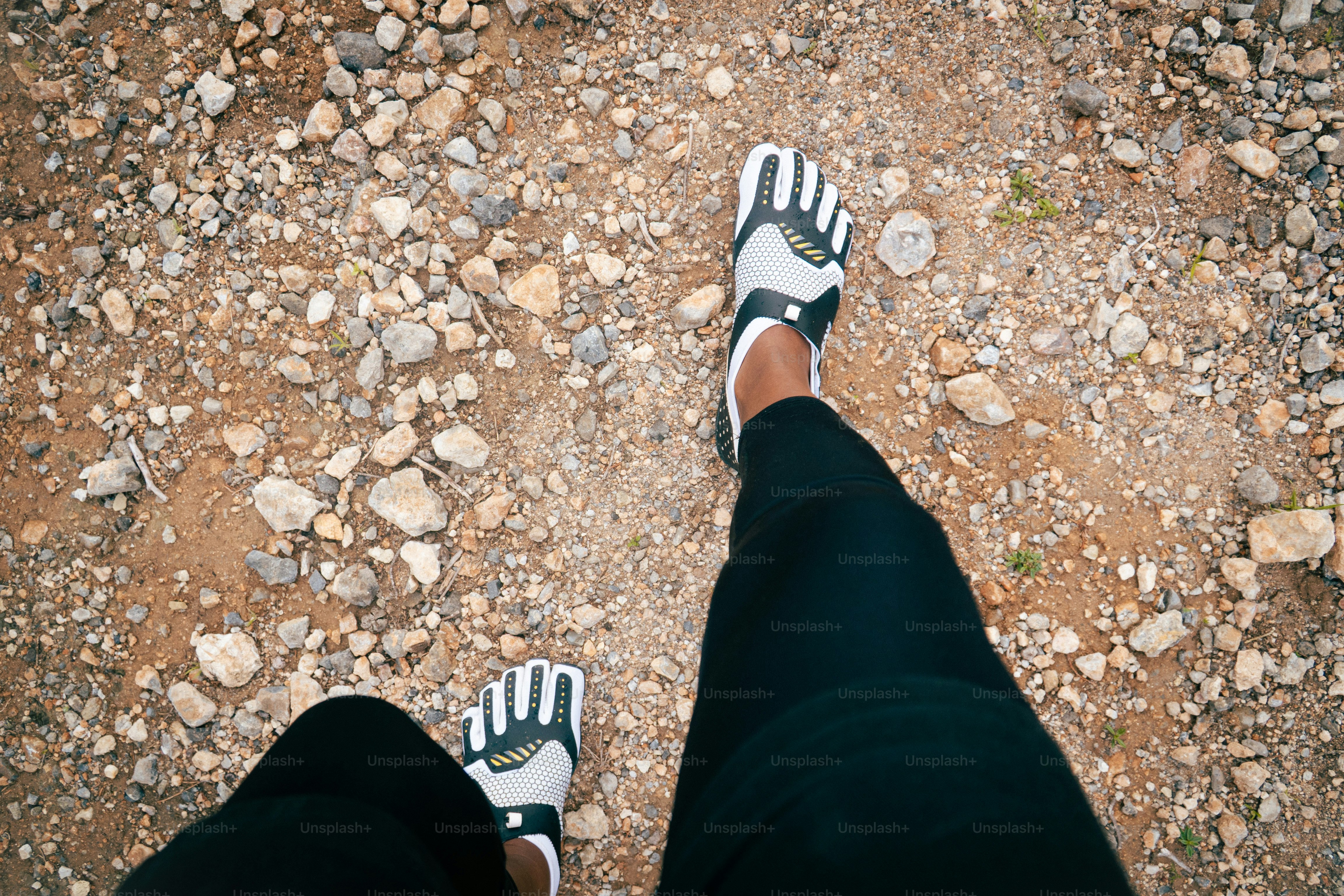 Person wearing minimalist shoes walking on gravel path.