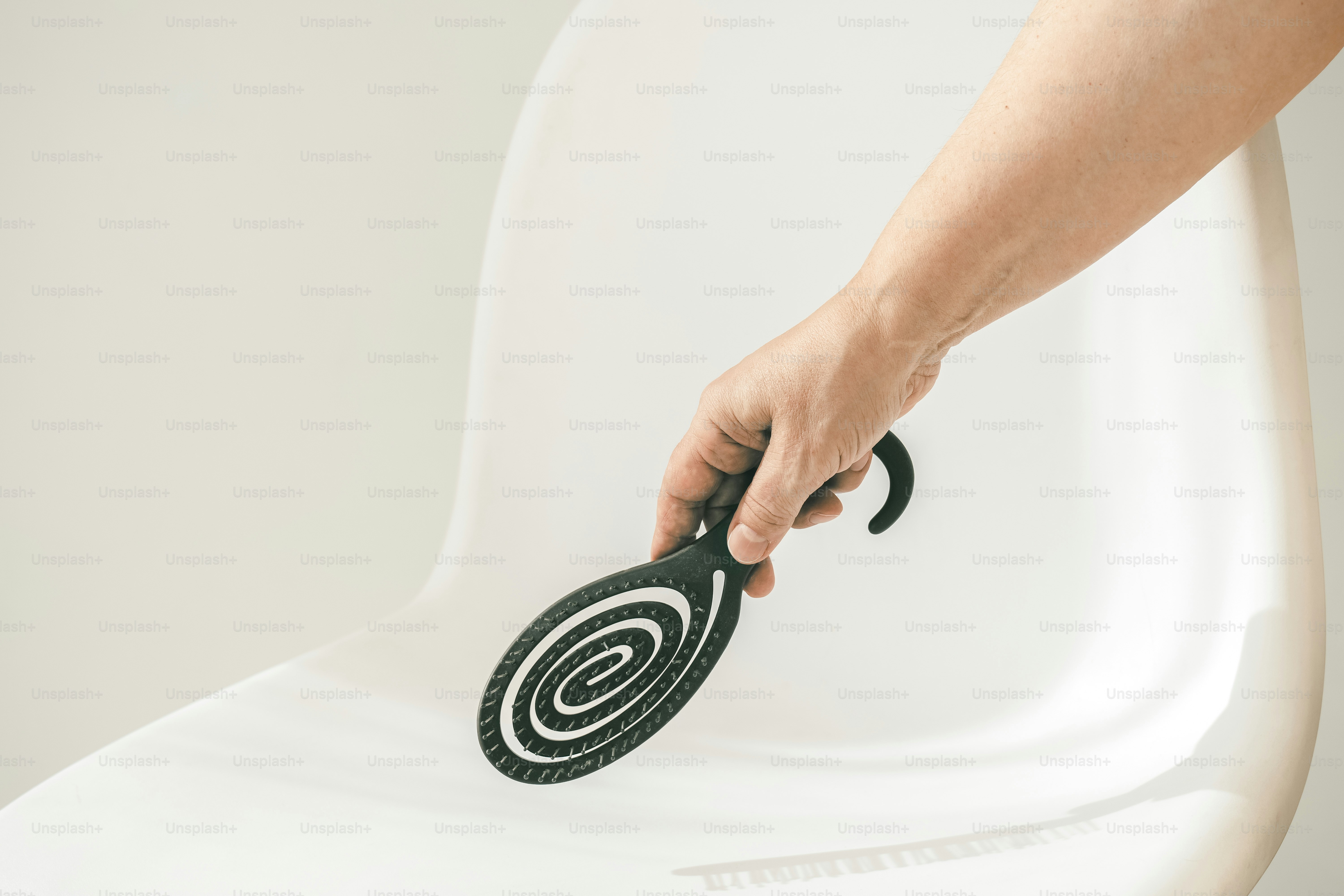 Hand holding a black spiral brush near white chair