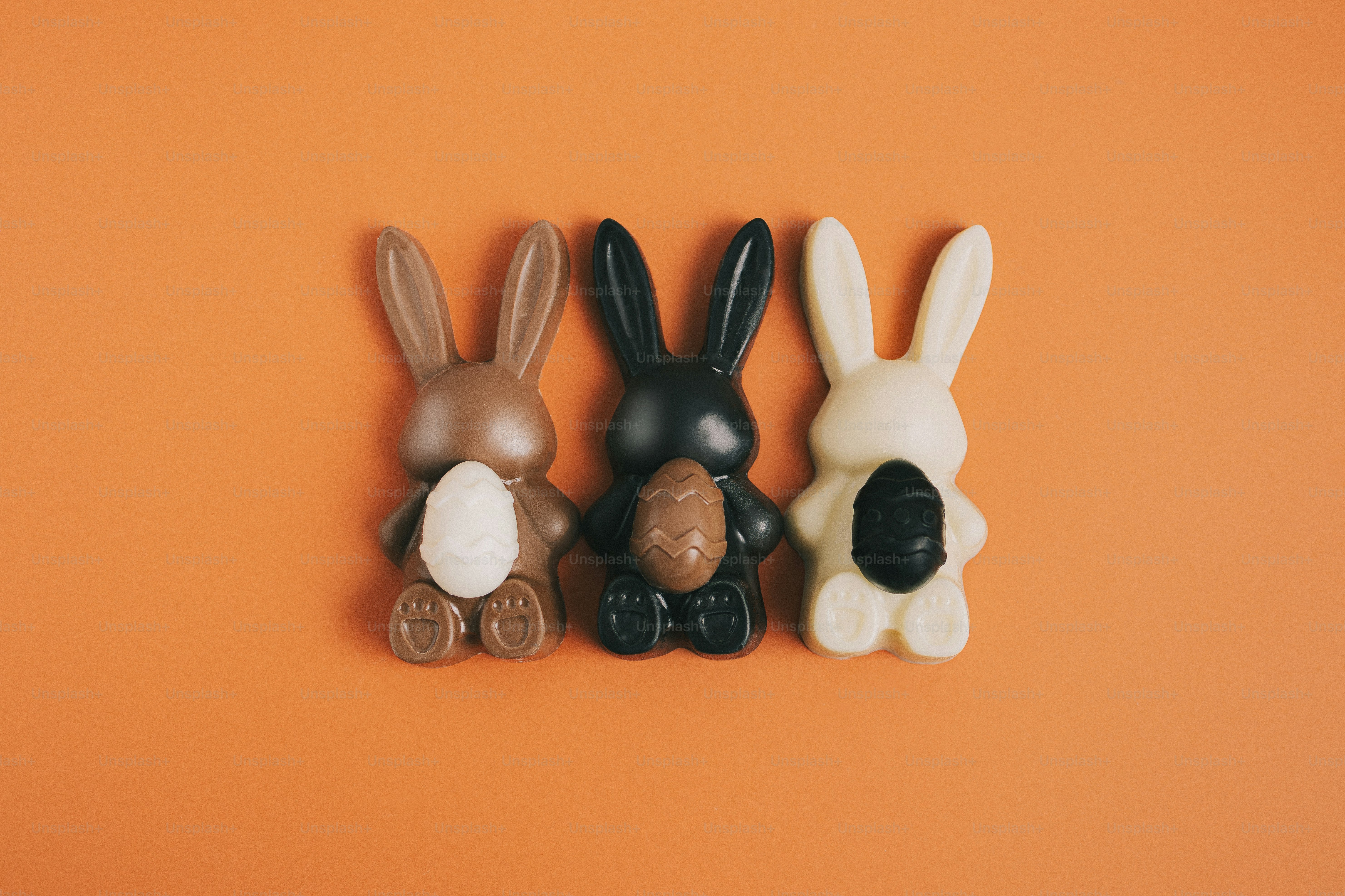 Three chocolate bunnies with eggs on orange background