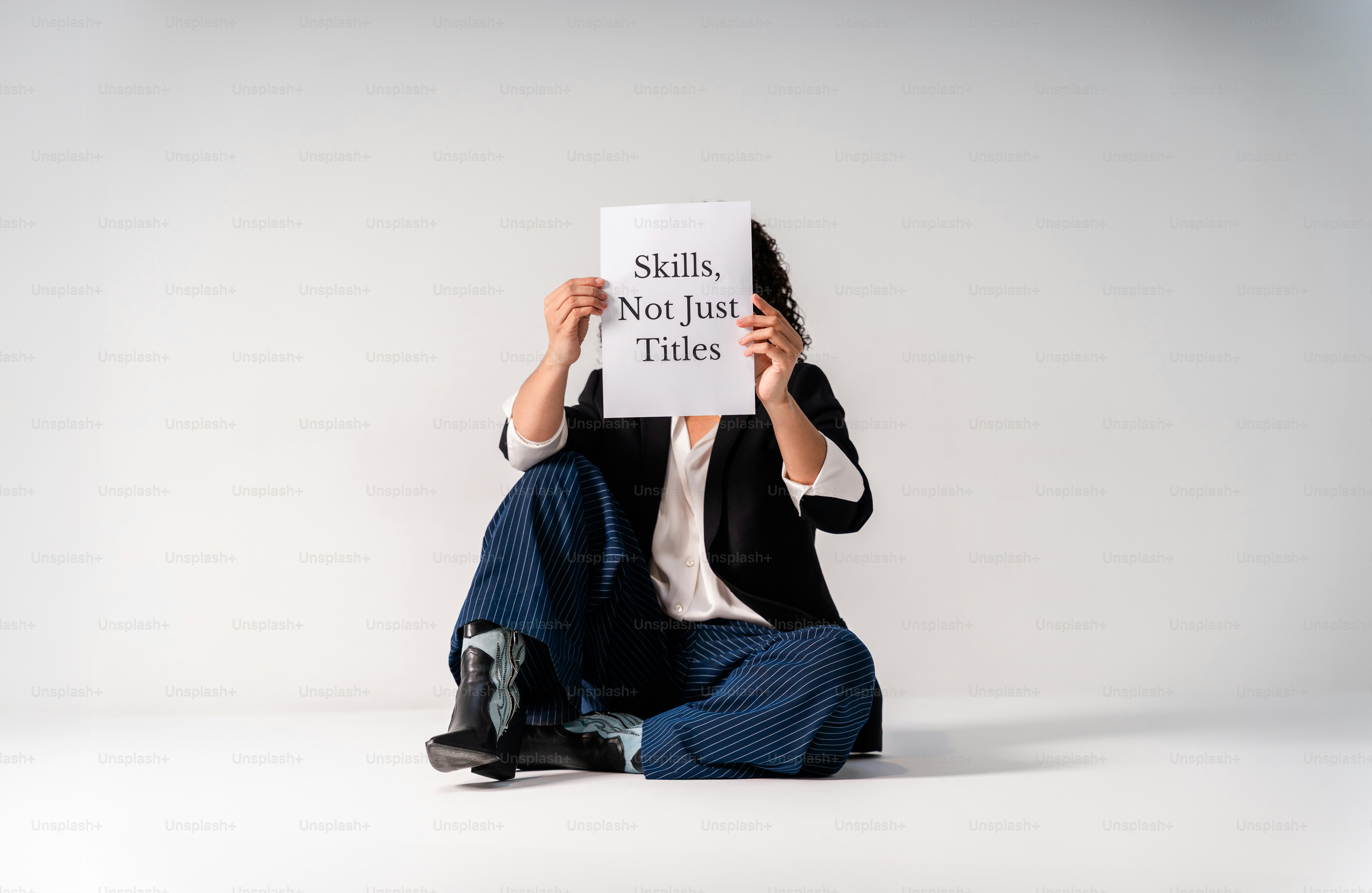 La persona è seduta con un foglio con un testo "competenze, non solo titoli"