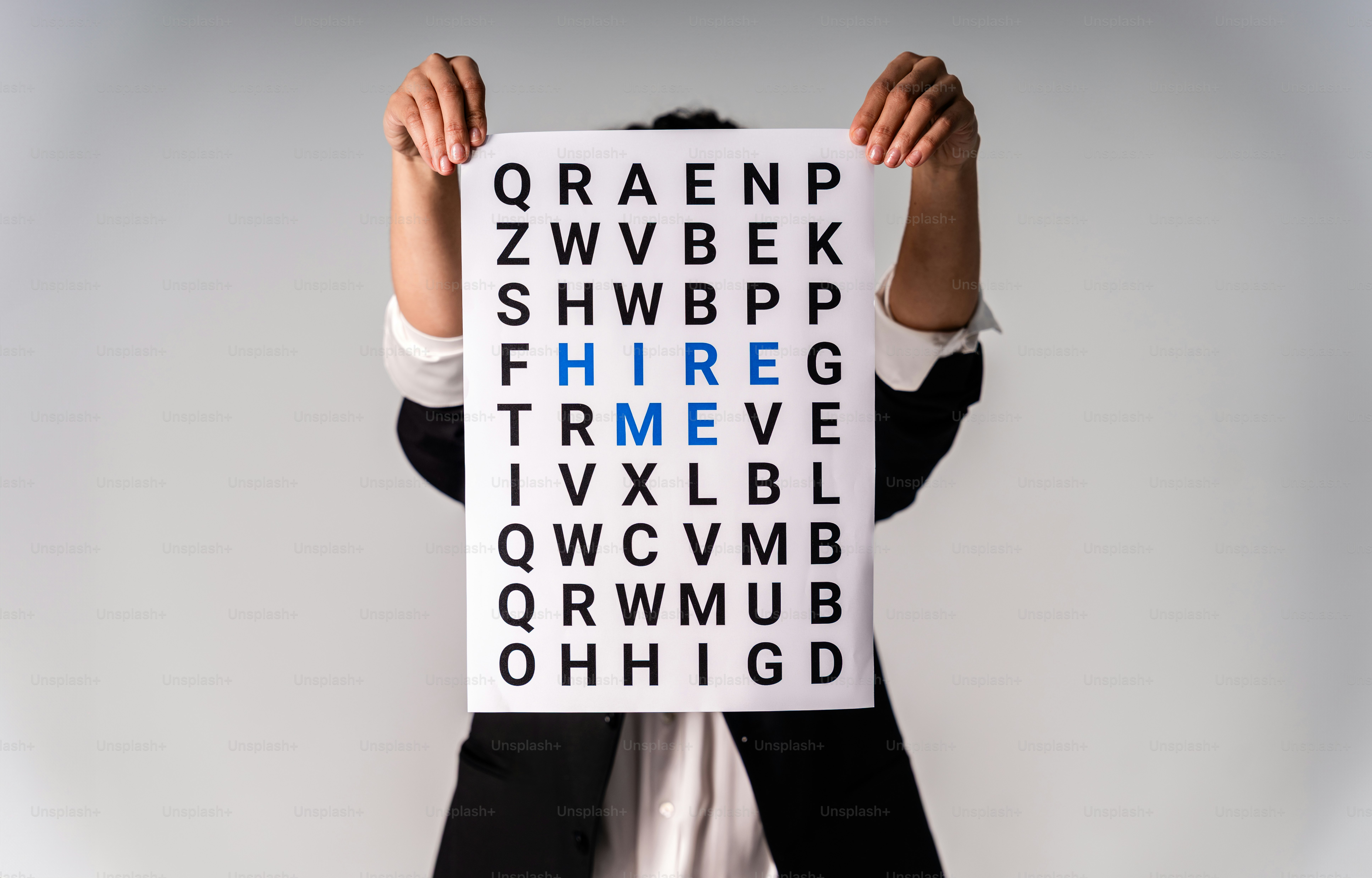 Person holding eye chart with "hire me" visible.