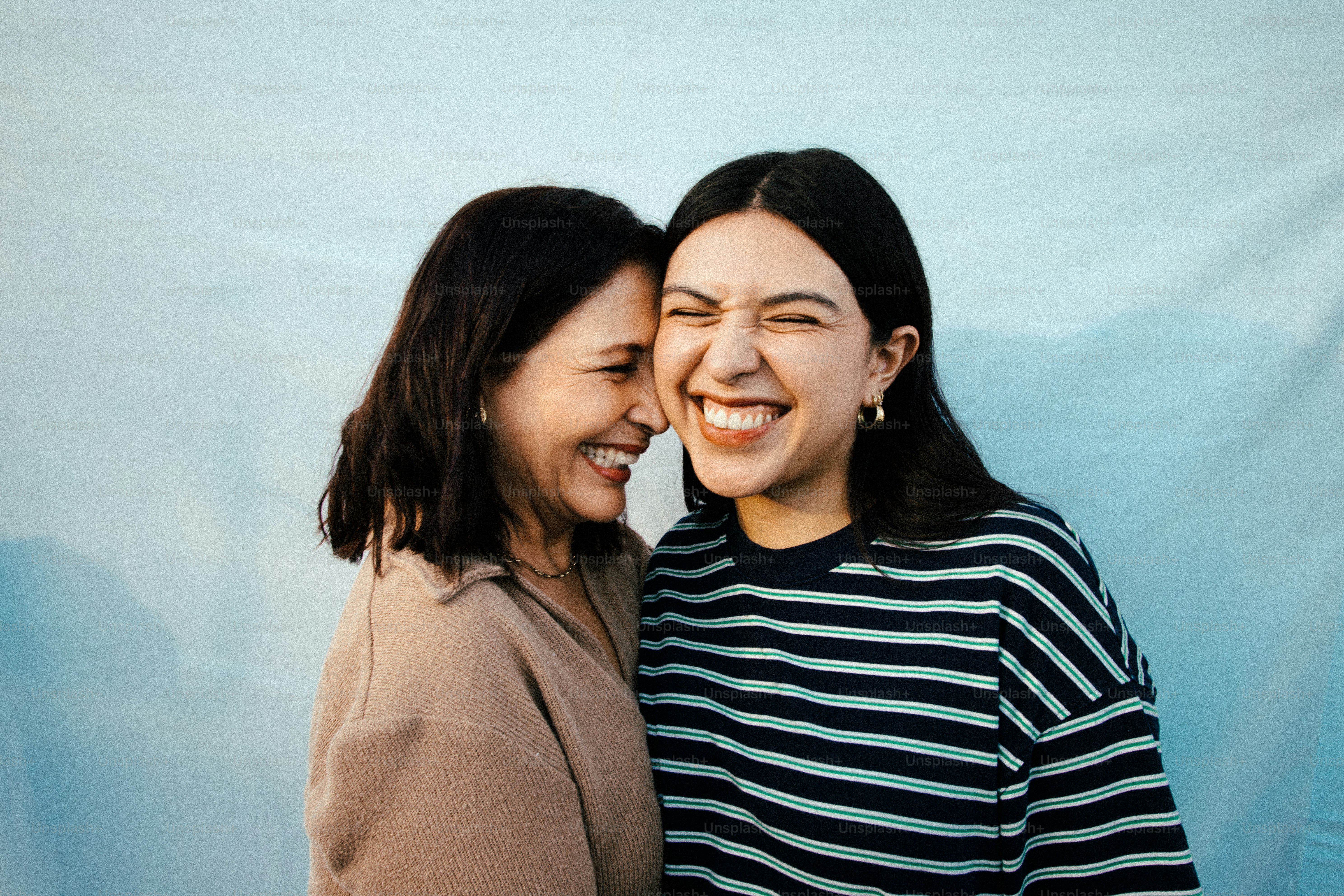 Two women laughing together against a blue backdrop