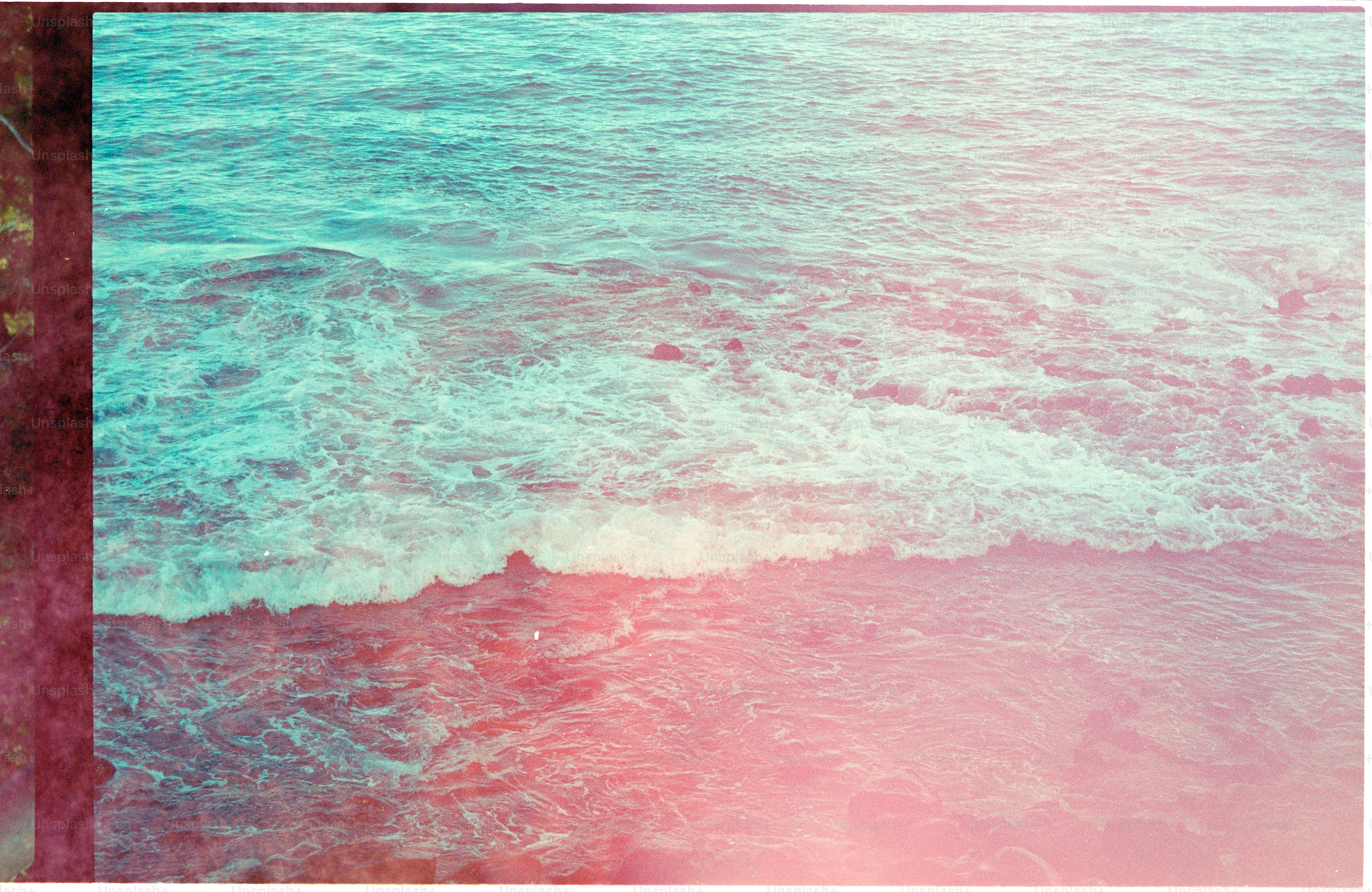 Turquoise ocean waves crashing on a pink-hued shore