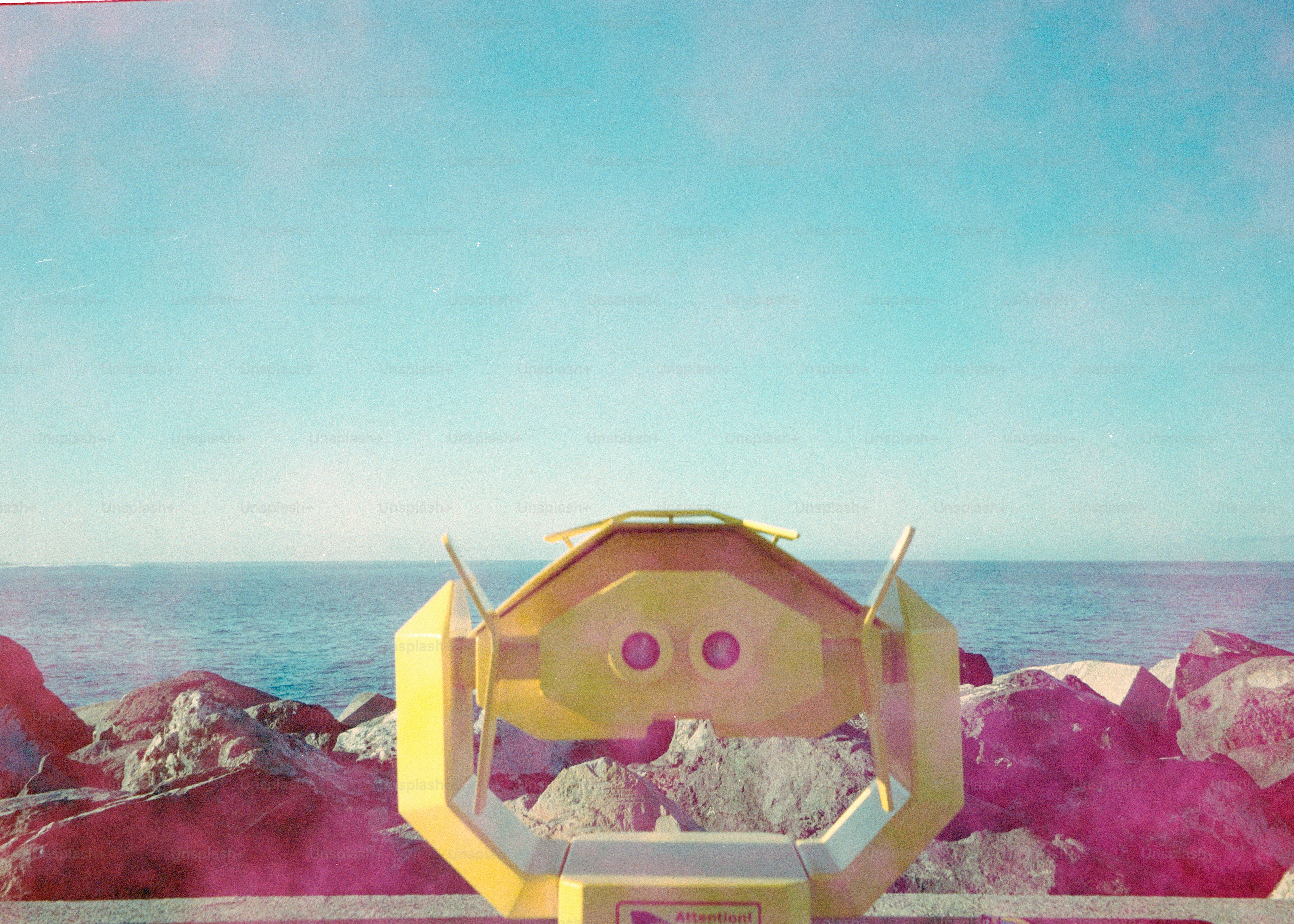 Yellow binocular viewer on rocky shore overlooking ocean