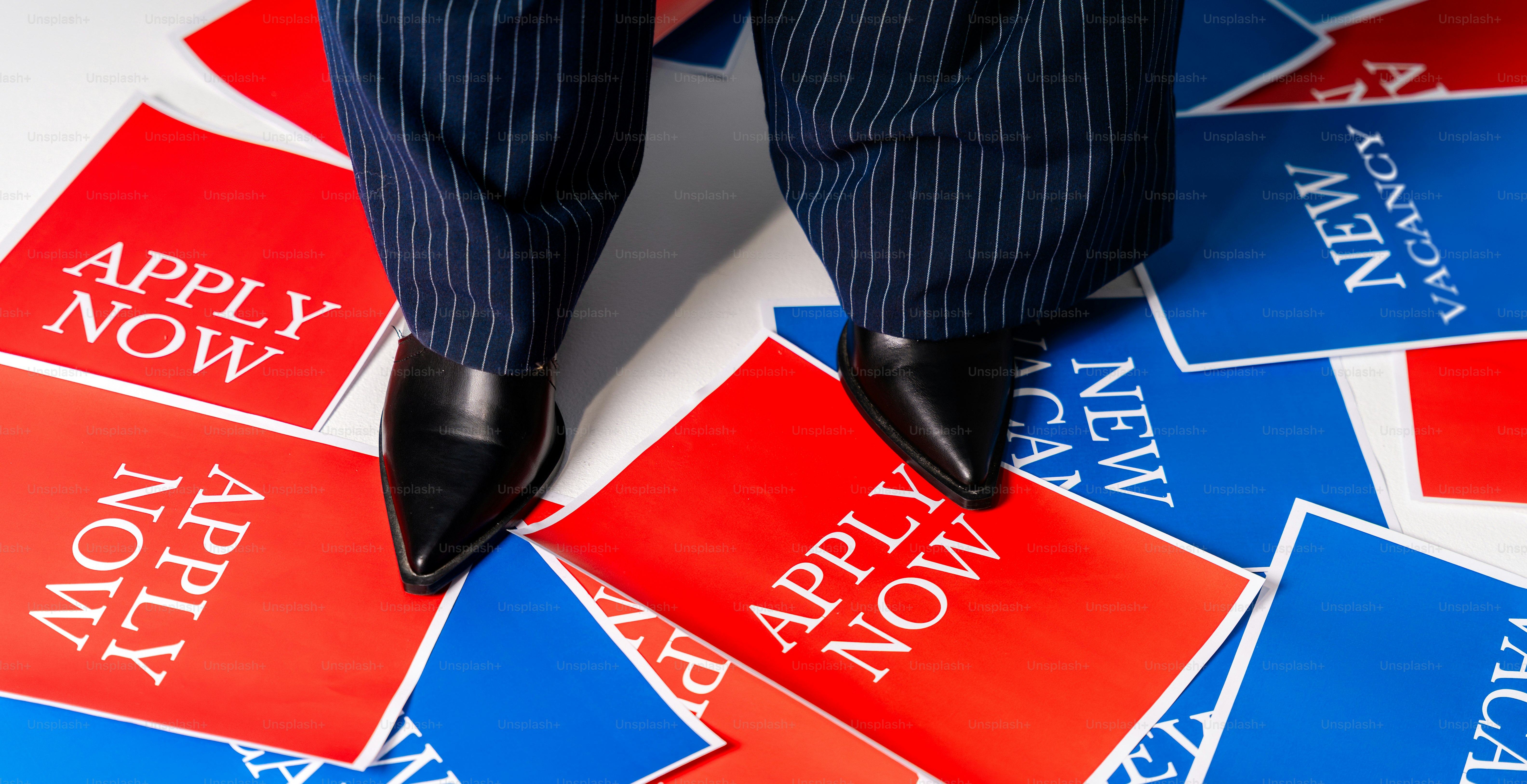 Person standing on 'apply now' and 'new vacancy' signs