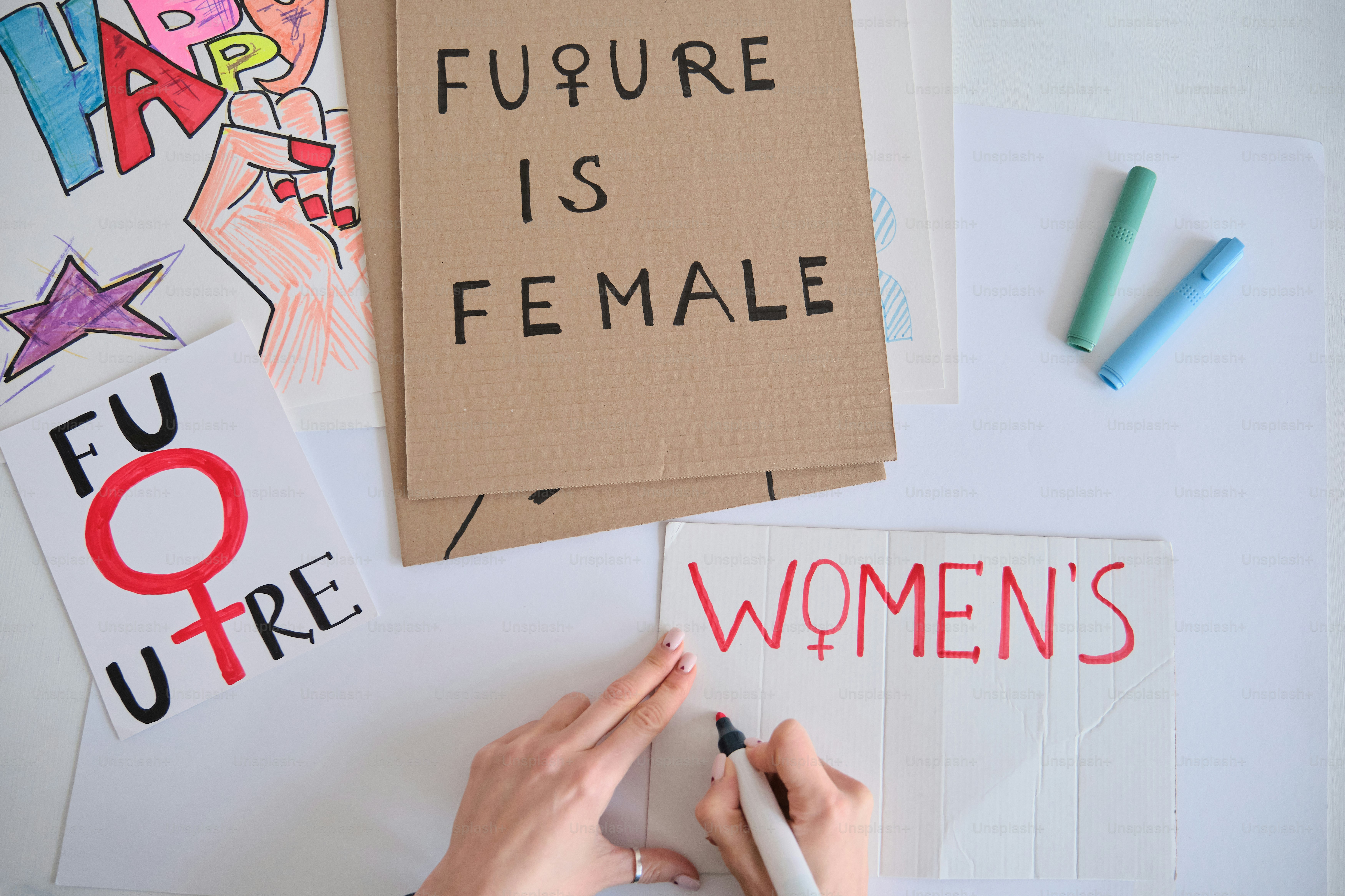 Hands writing "women's" next to feminist signs.