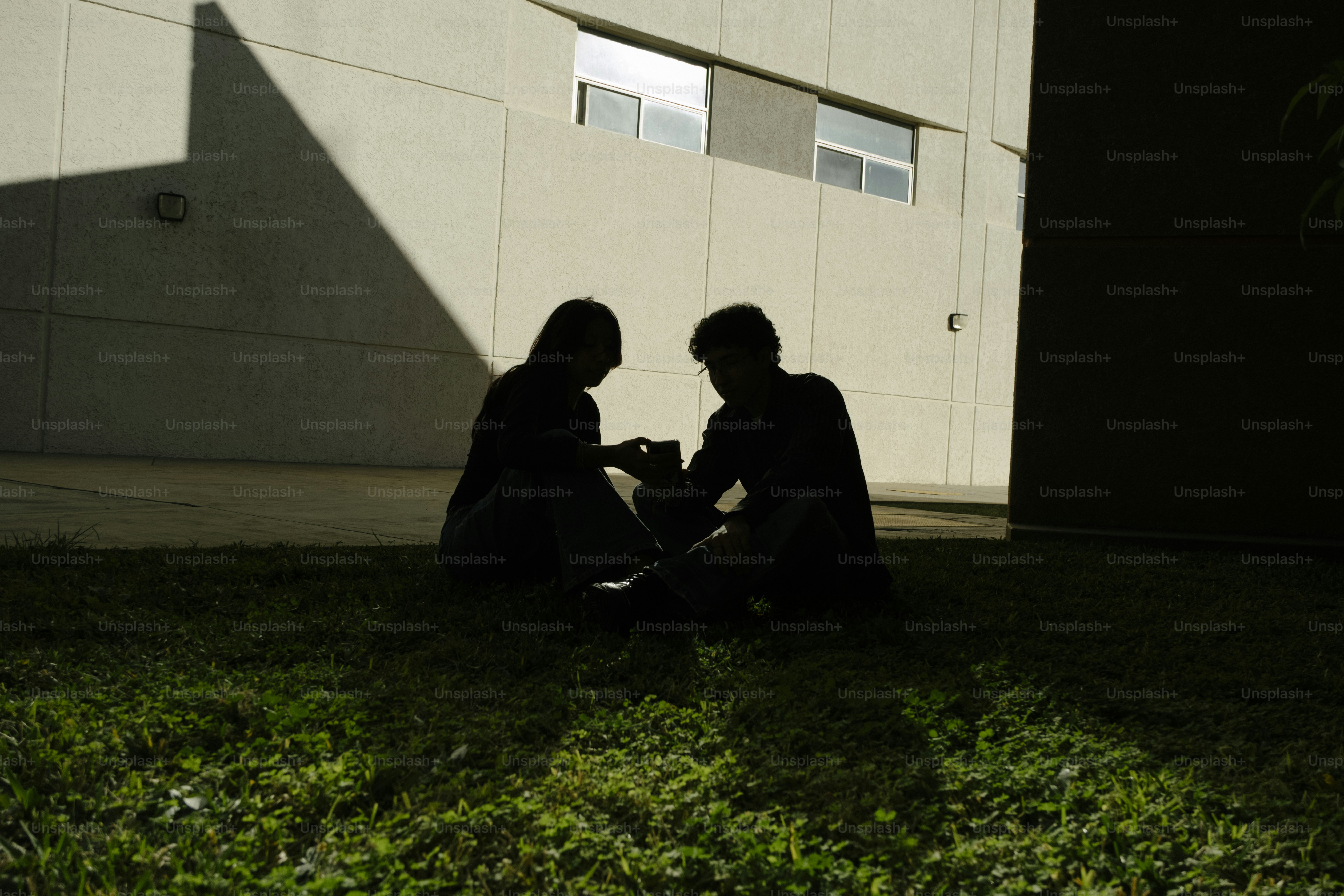 Two people sit in the grass in shadow