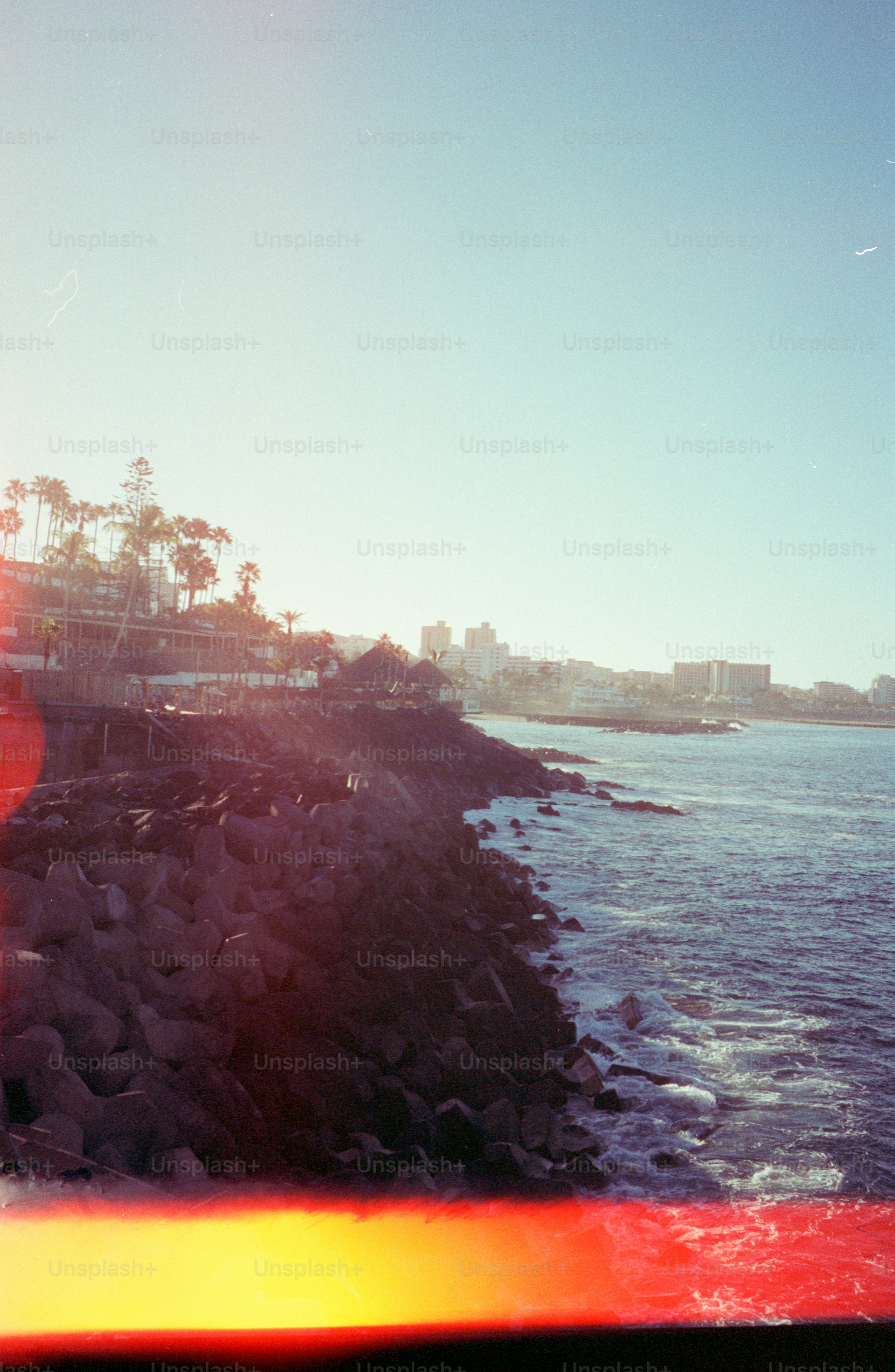 Rocky coastline with waves crashing and buildings in distance.