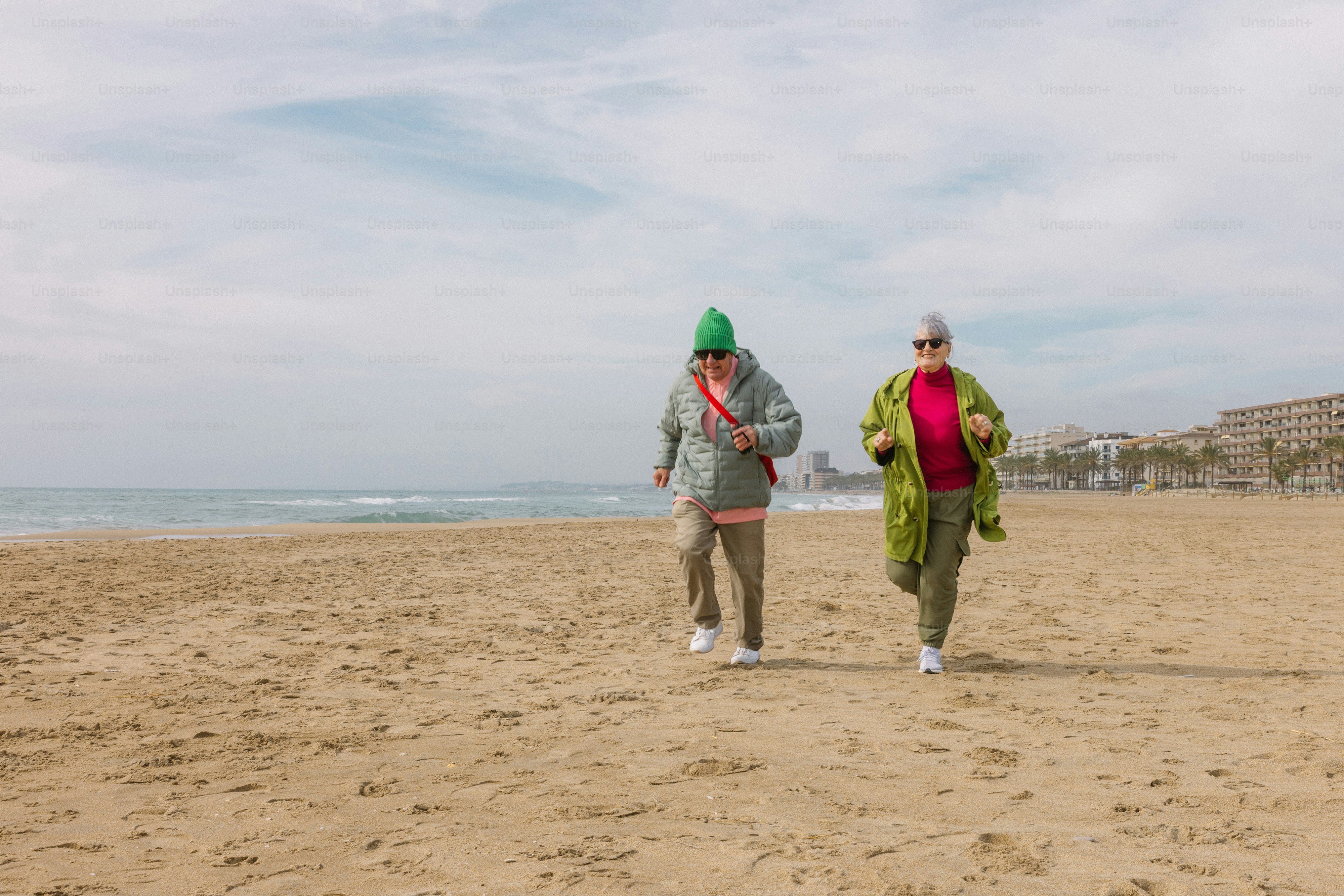 Duas mulheres correndo em uma praia de areia perto do oceano.