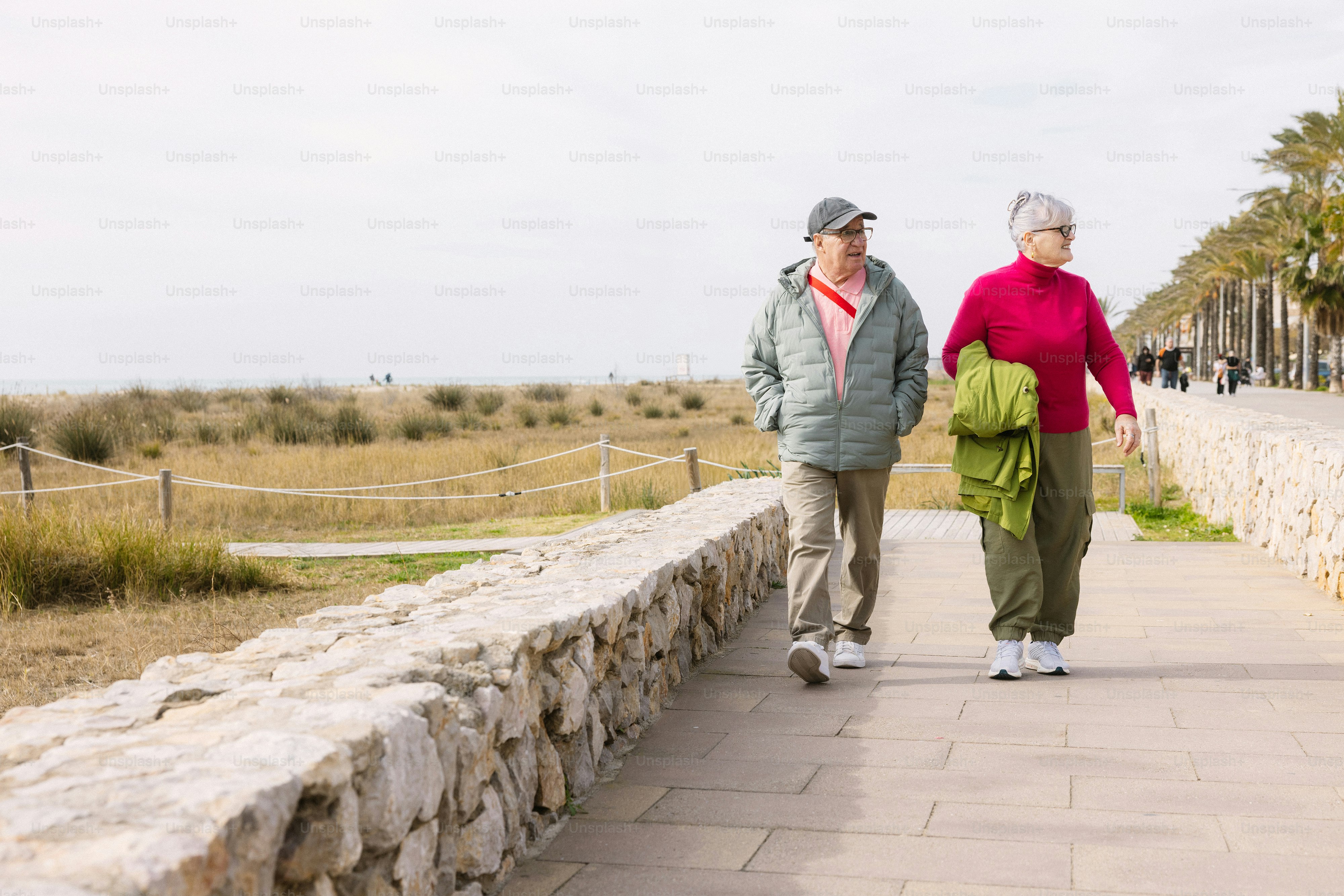Casal idoso caminhando por um caminho pavimentado à beira-mar.