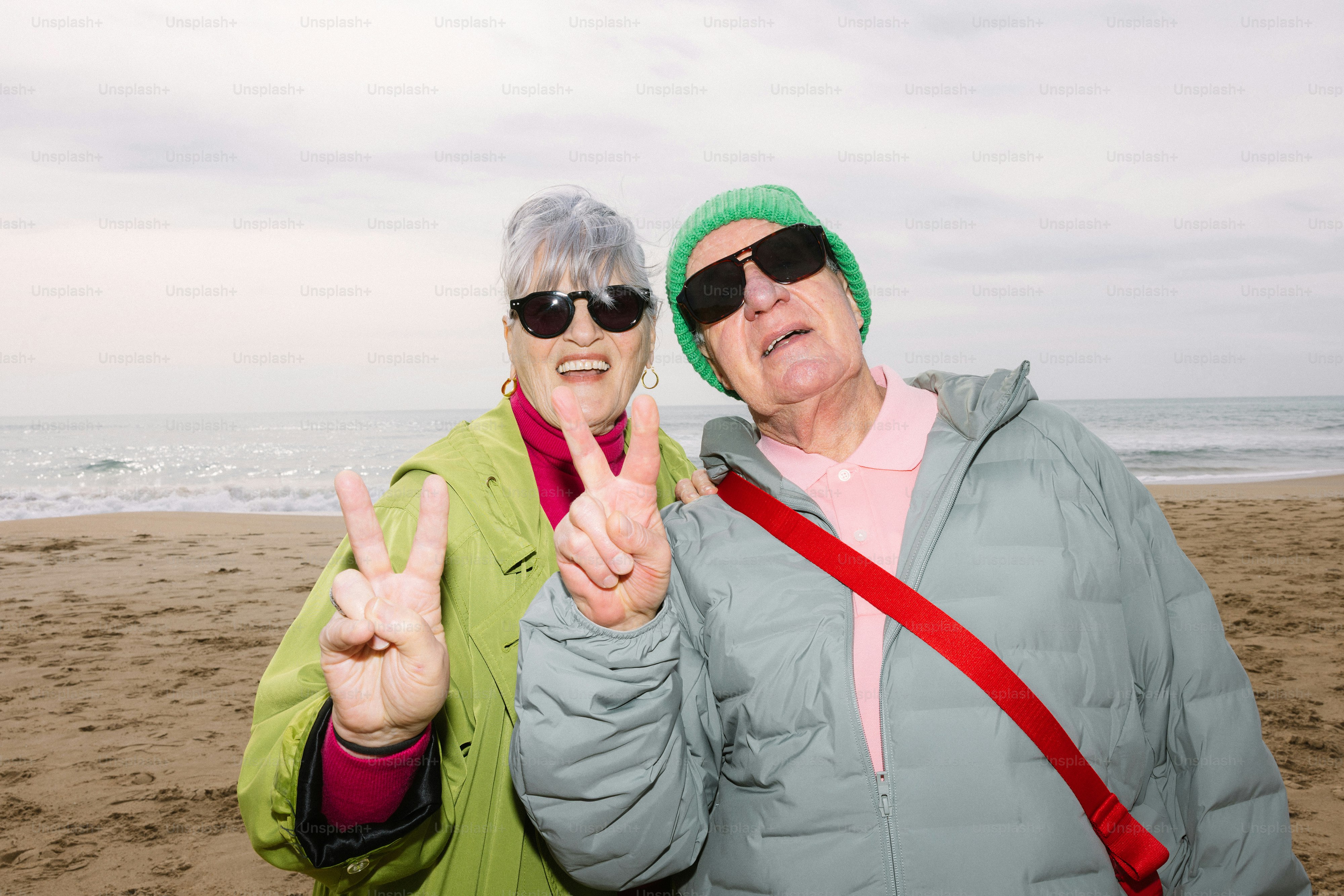 Dois idosos sorridentes fazendo sinais de paz na praia