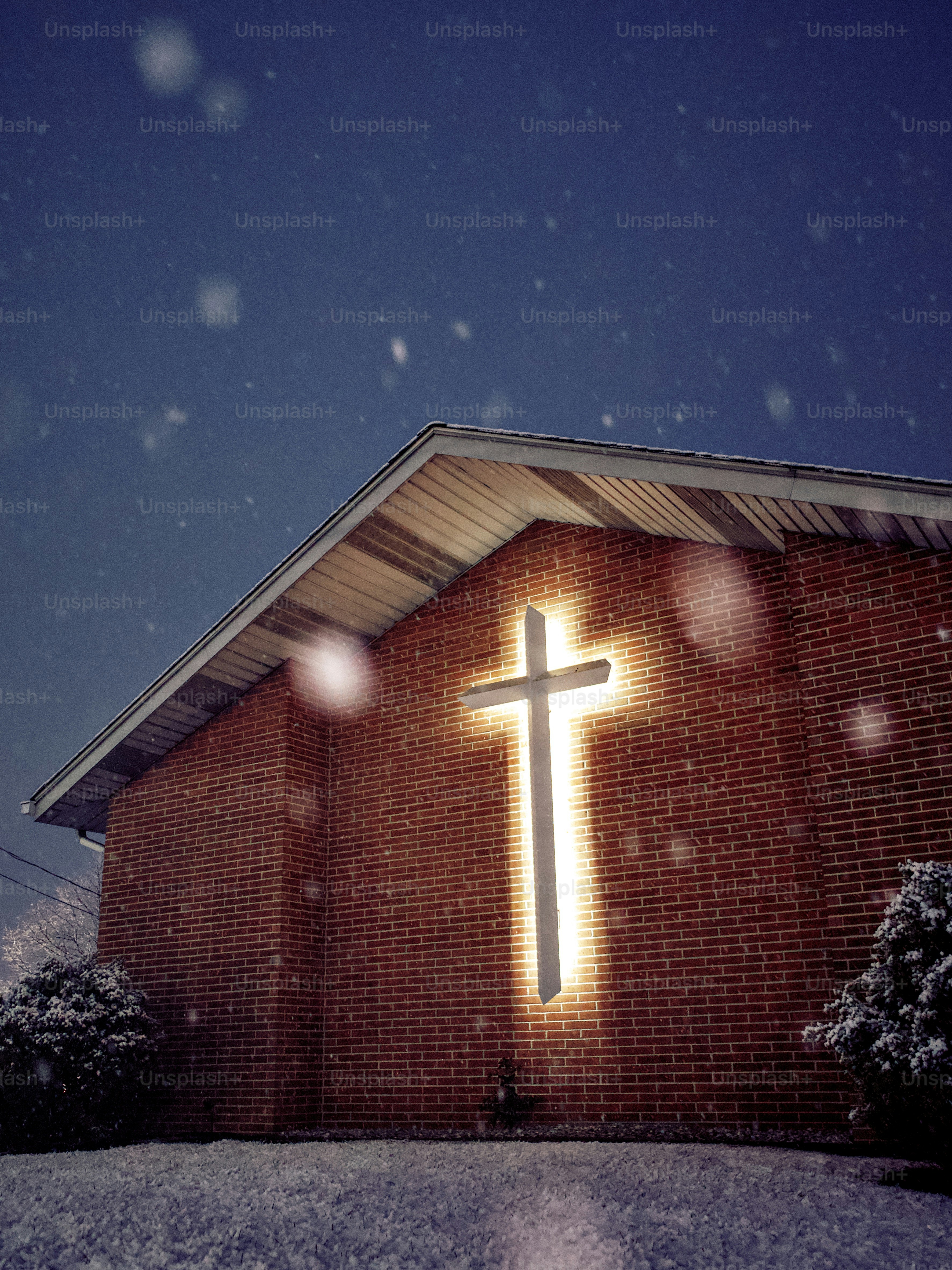 Glowing cross on brick church during snowfall