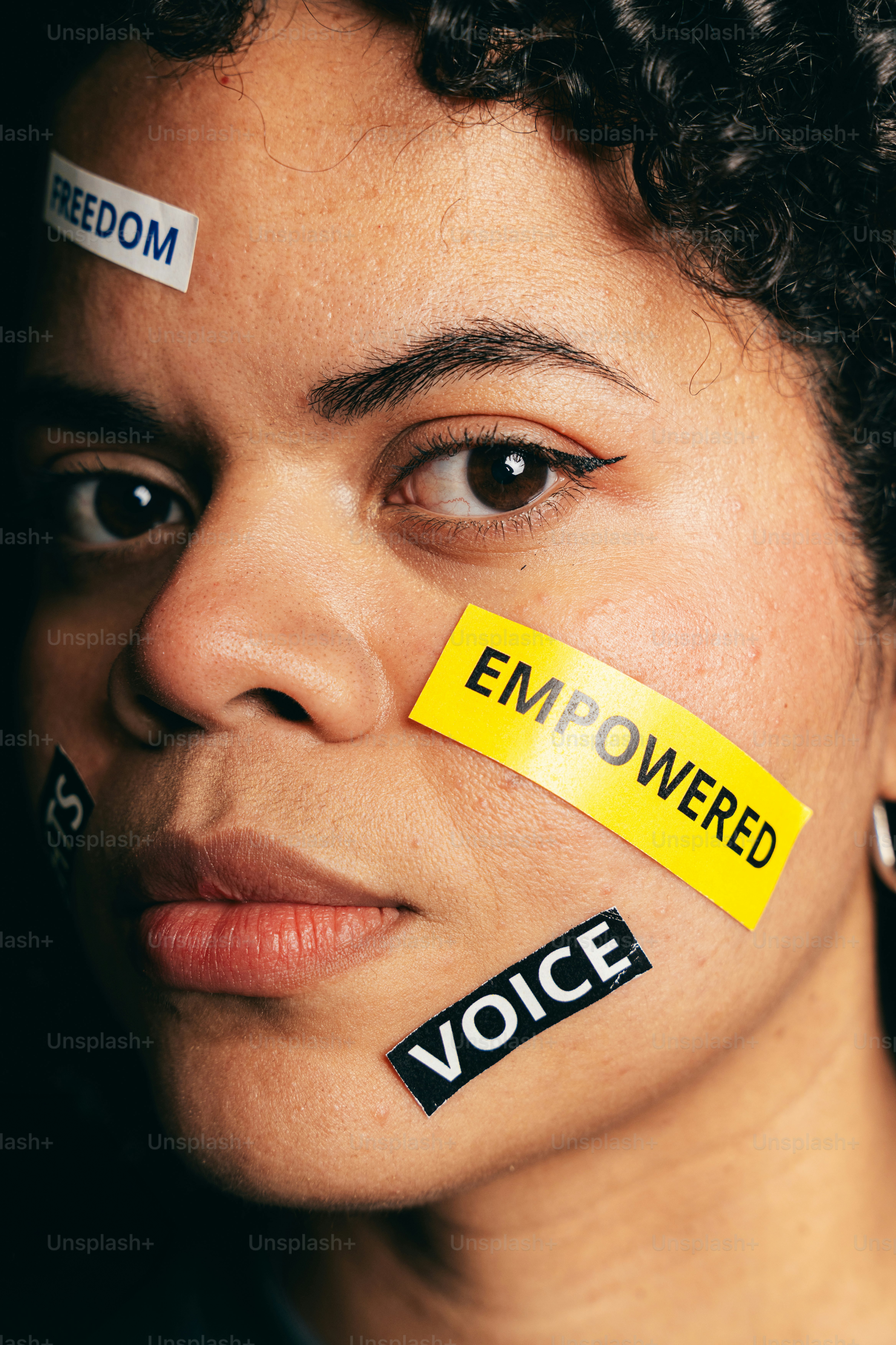 Woman with "empowered", "freedom", and "voice" stickers on face.
