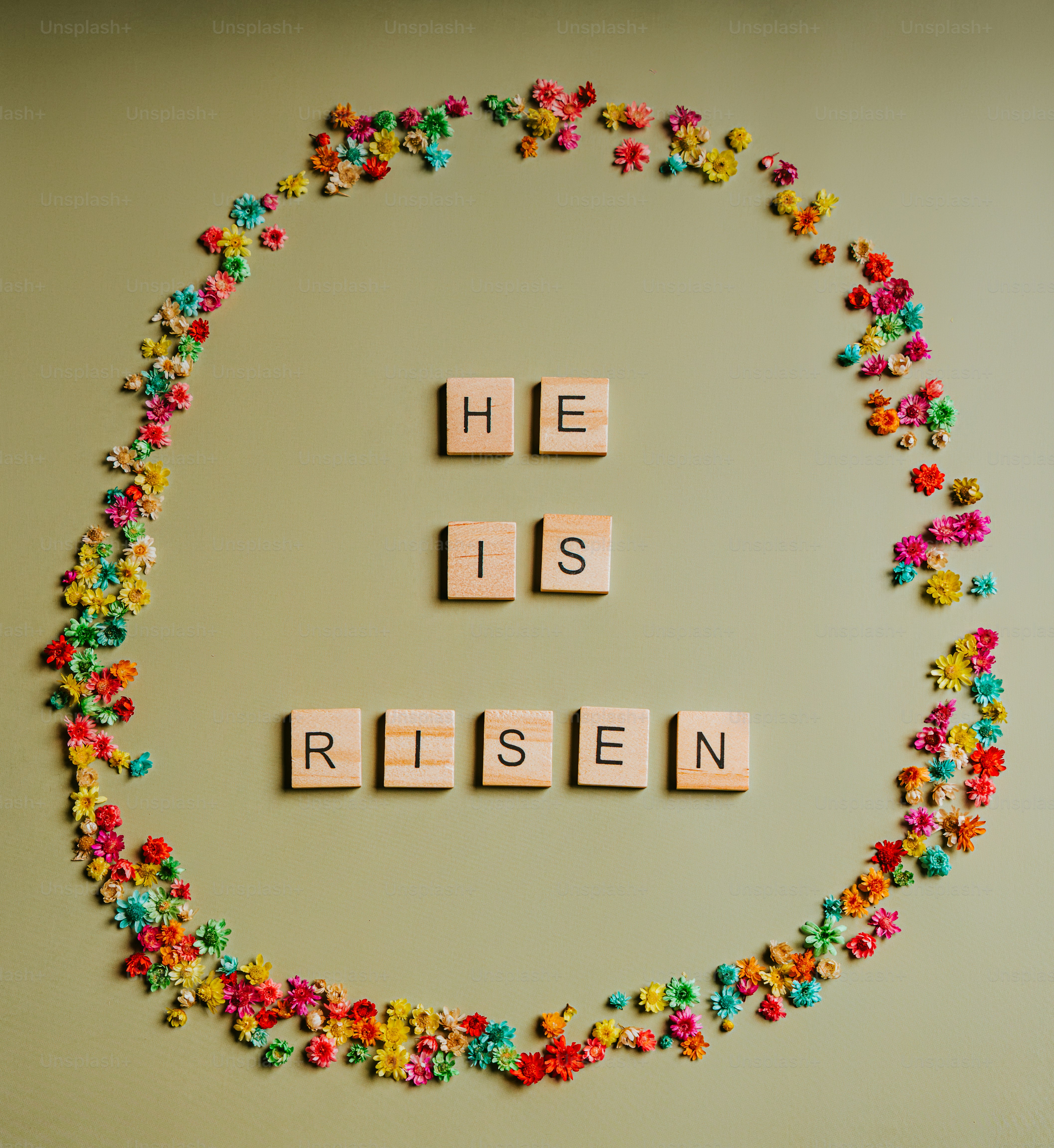 Scrabble tiles spell out 'he is risen' surrounded by flowers