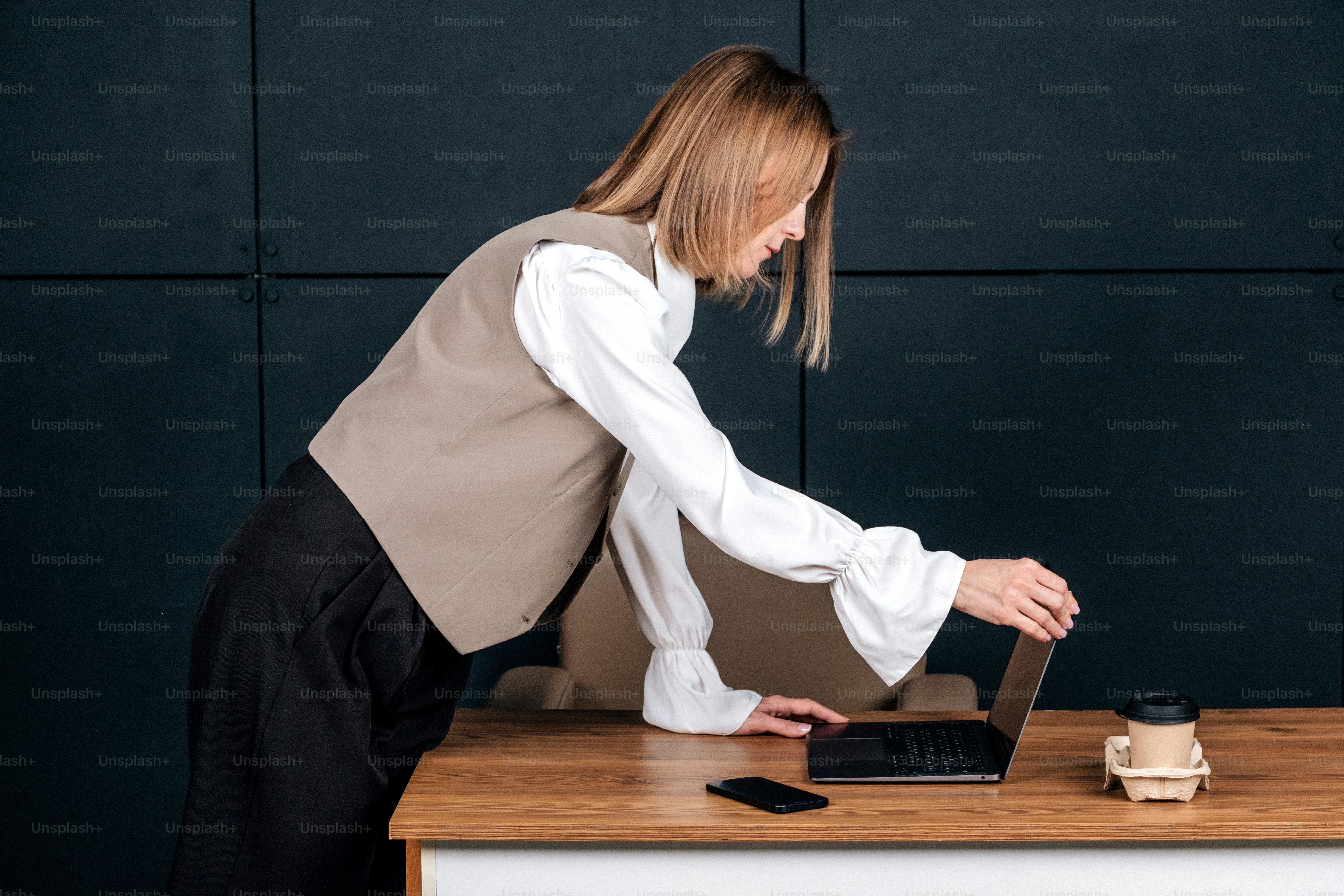 Woman in vest opening laptop at wooden desk