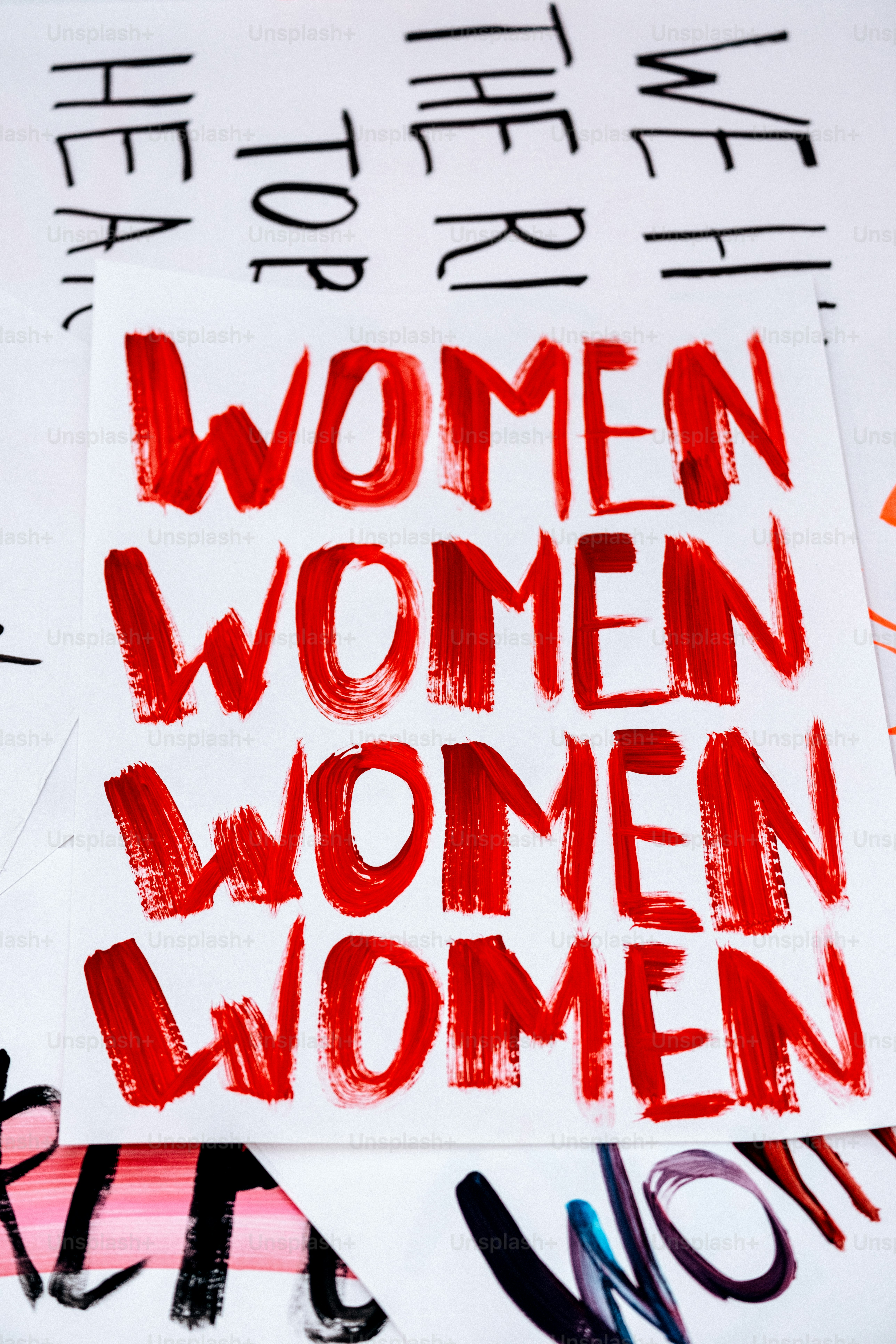 Des mots peints en rouge répétés par des femmes sur du papier blanc.