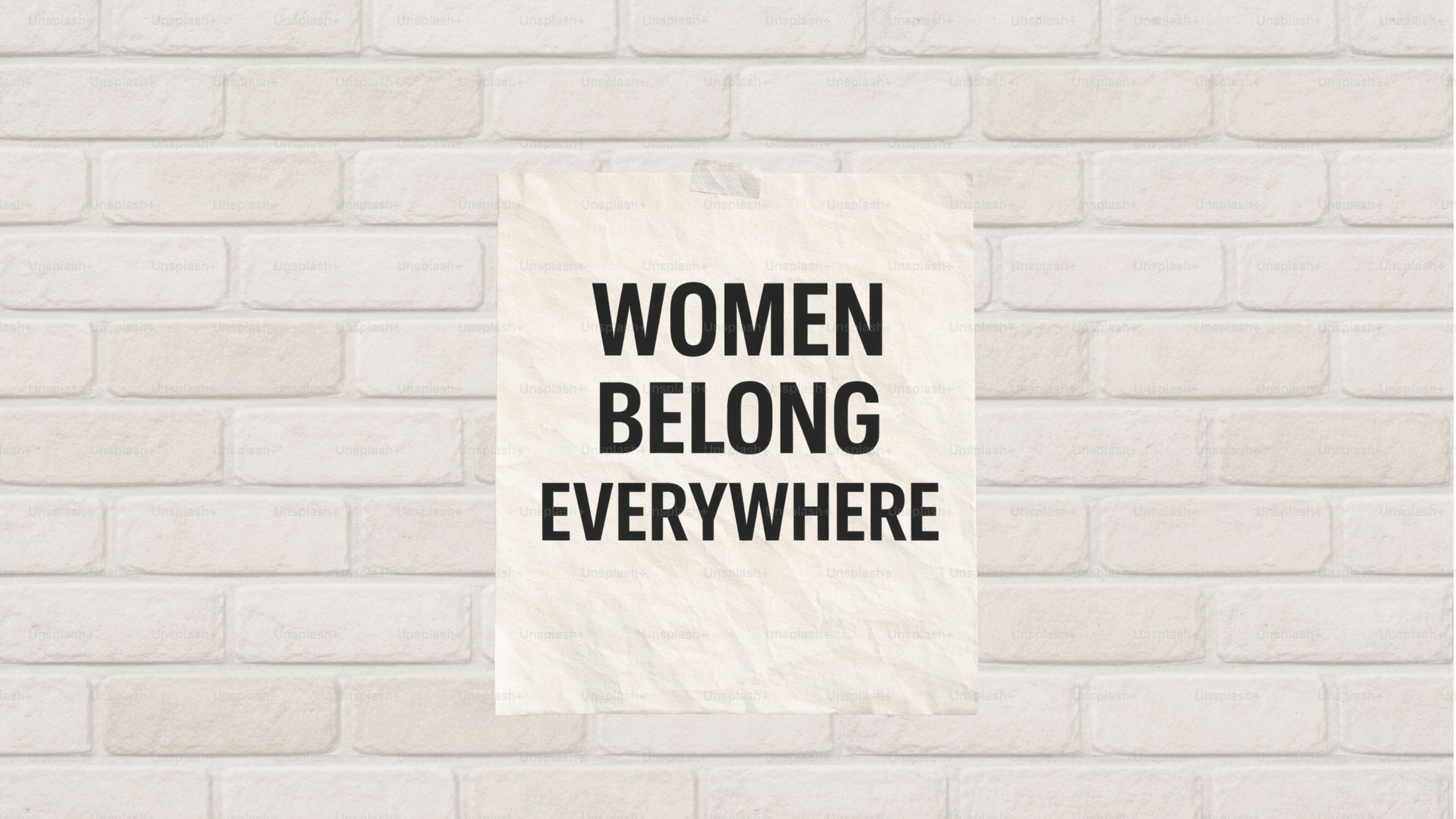 Poster with "women belong everywhere" text on brick wall