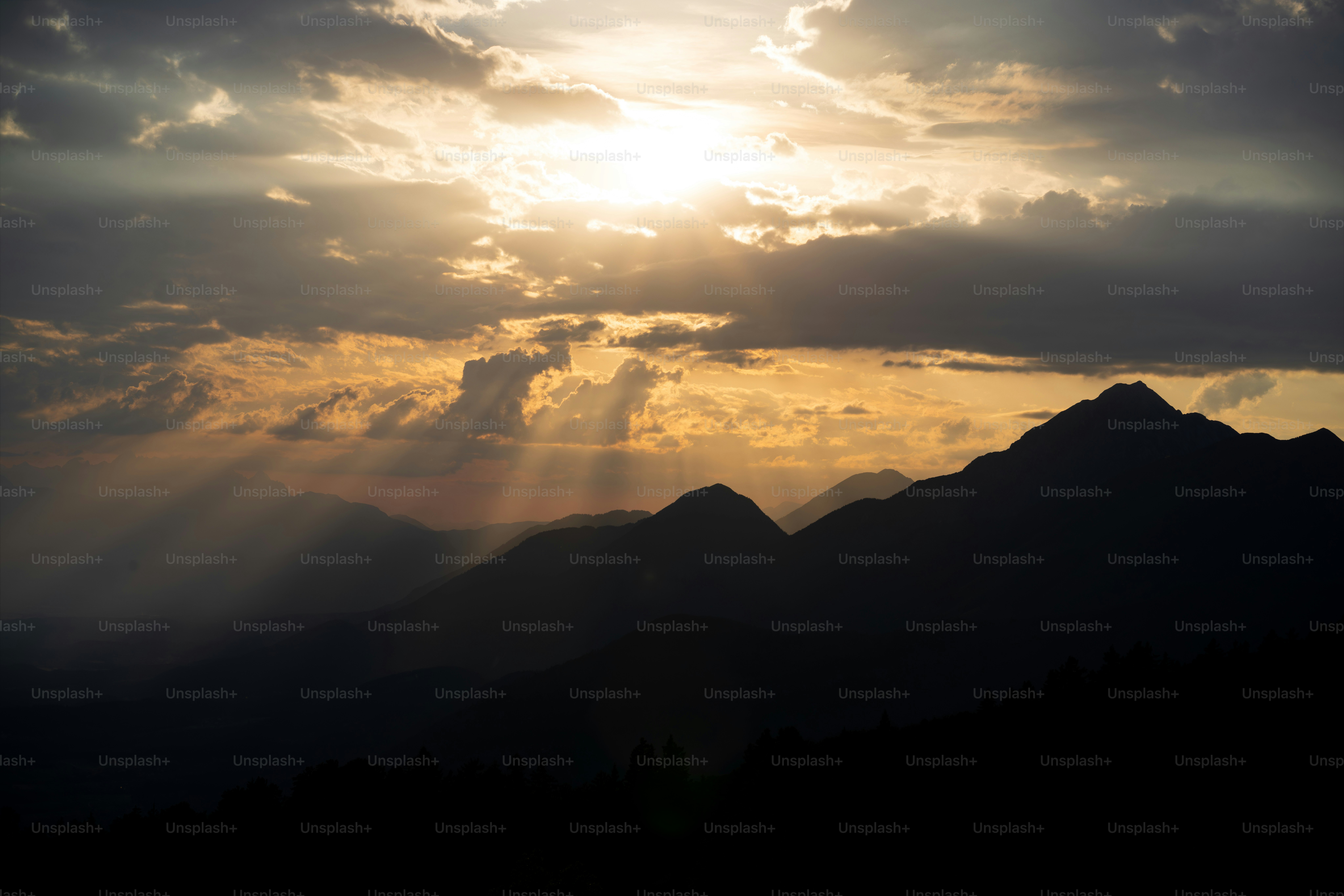 暗い山頂の上を雲の間から差し込む陽光。