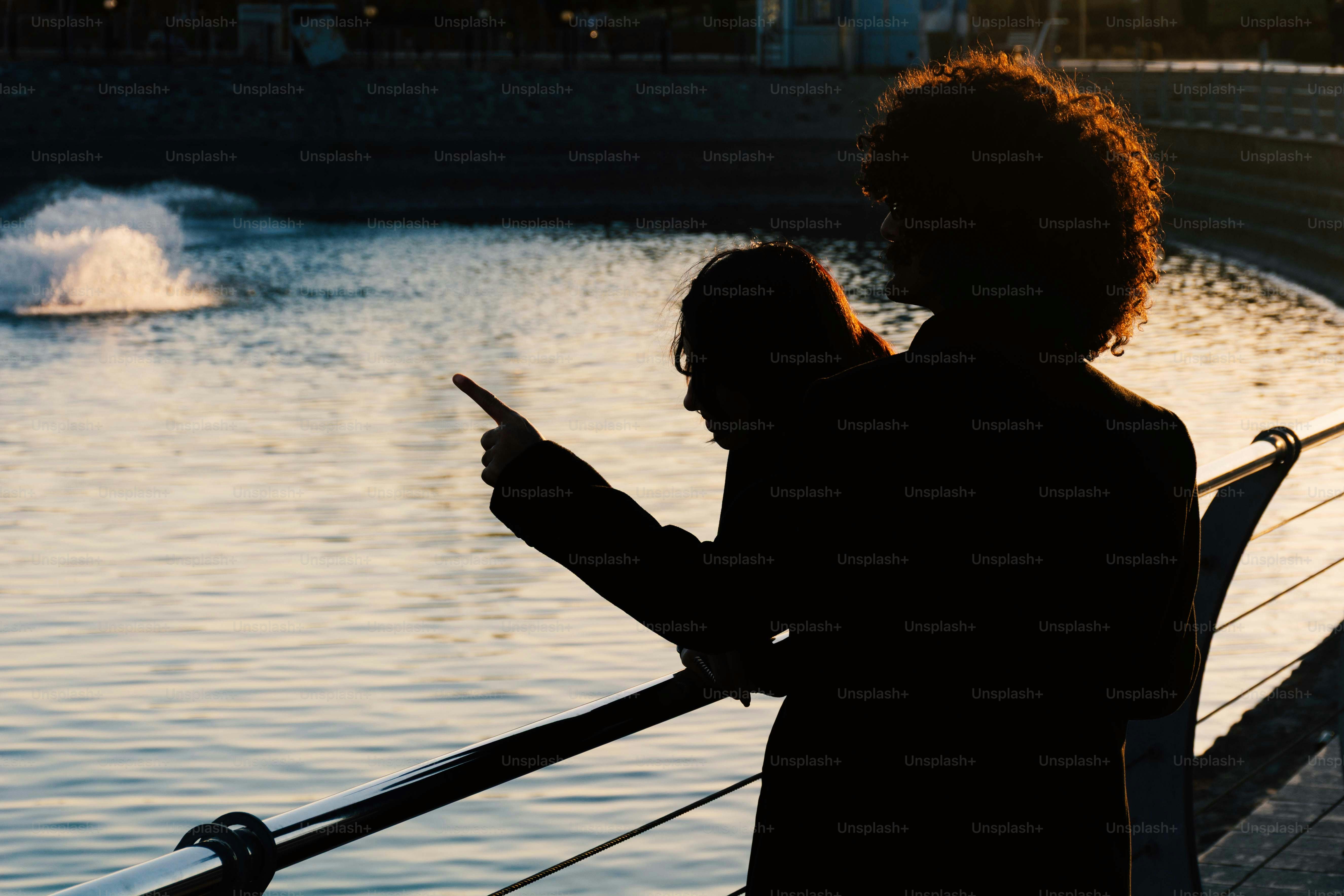 Dos personas señalando una fuente junto al agua.