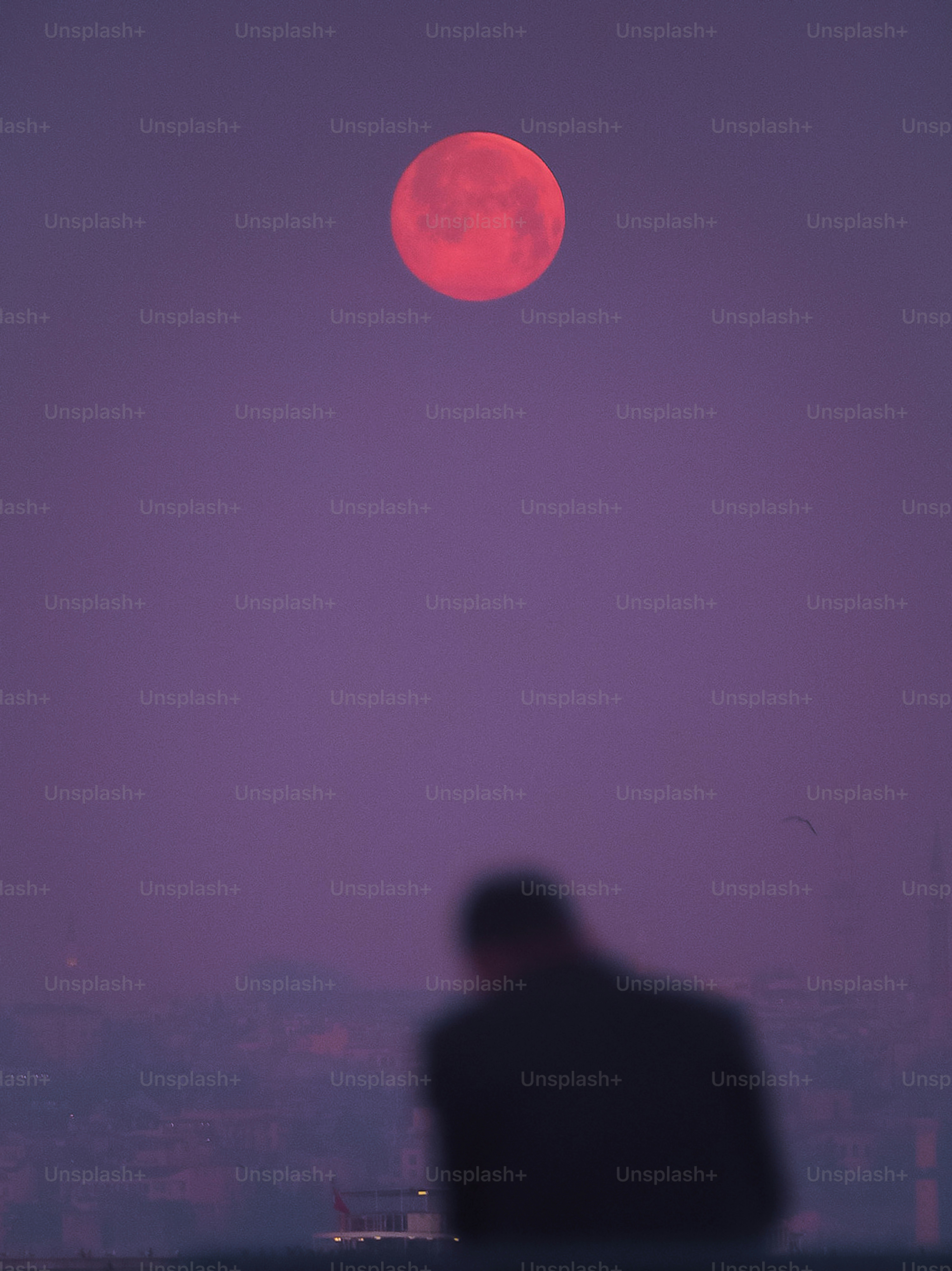 A person watches a large red moon in the sky.