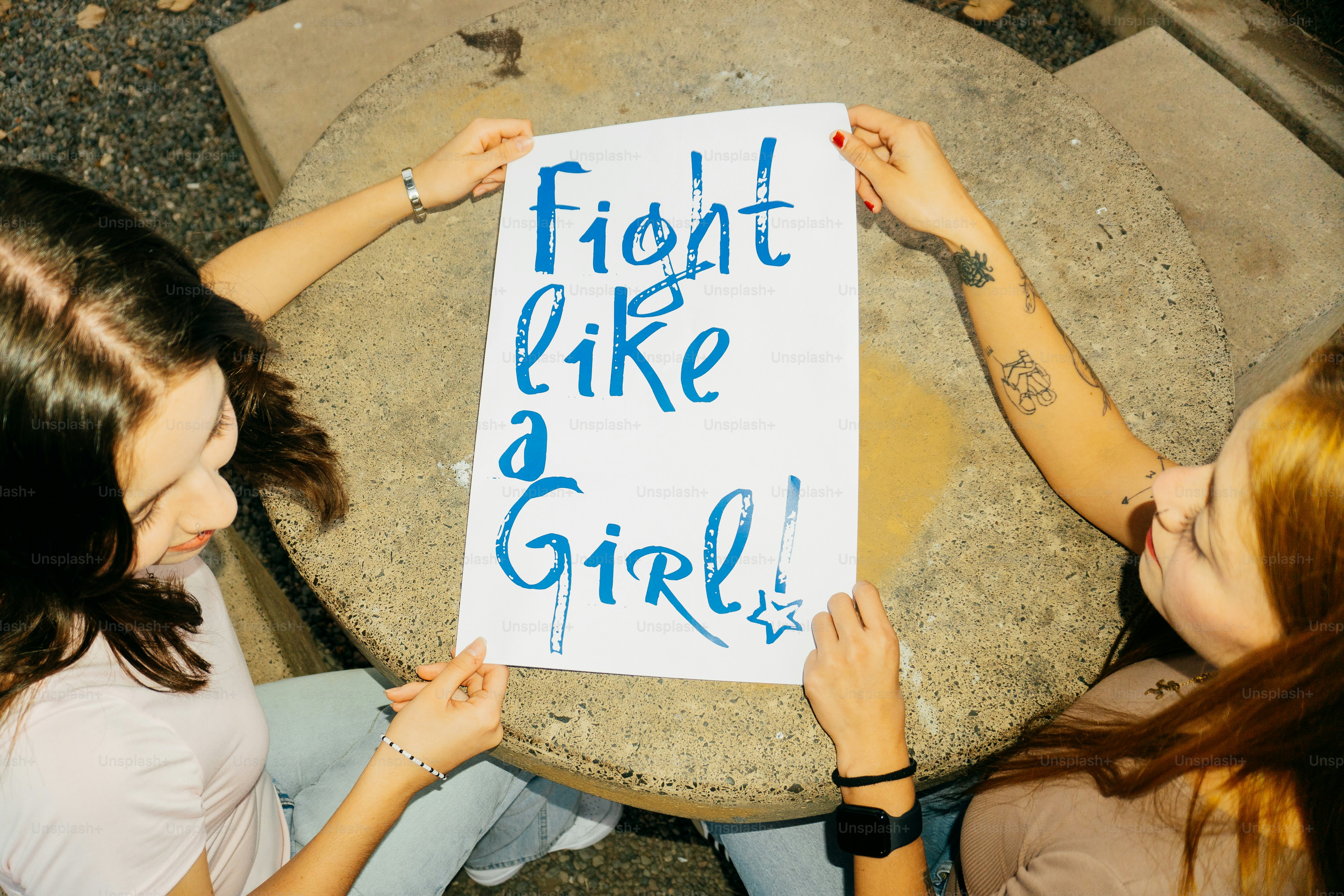 Two women hold a sign saying "fight like a girl!"