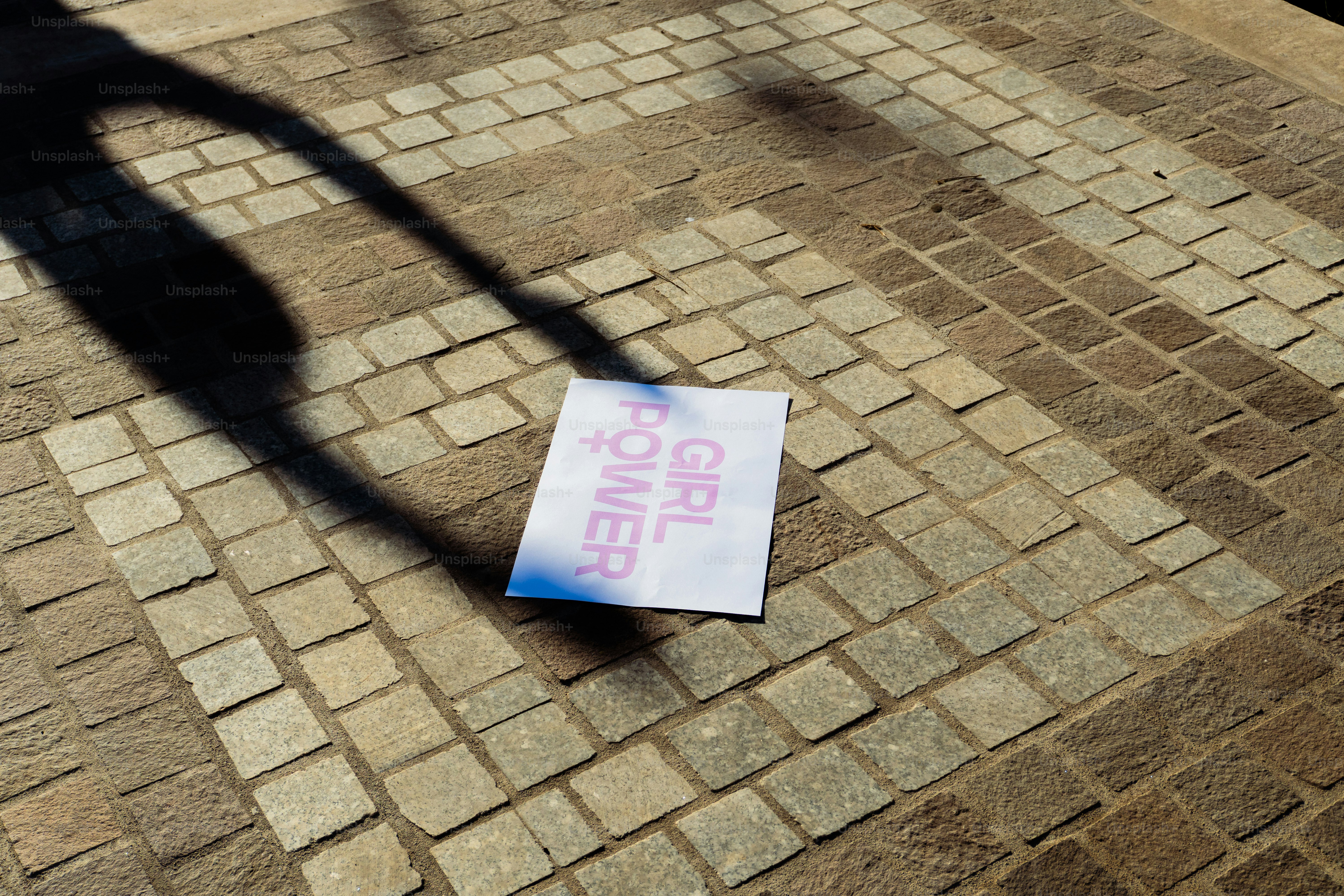A sign with "girl power" lies on a cobblestone path.
